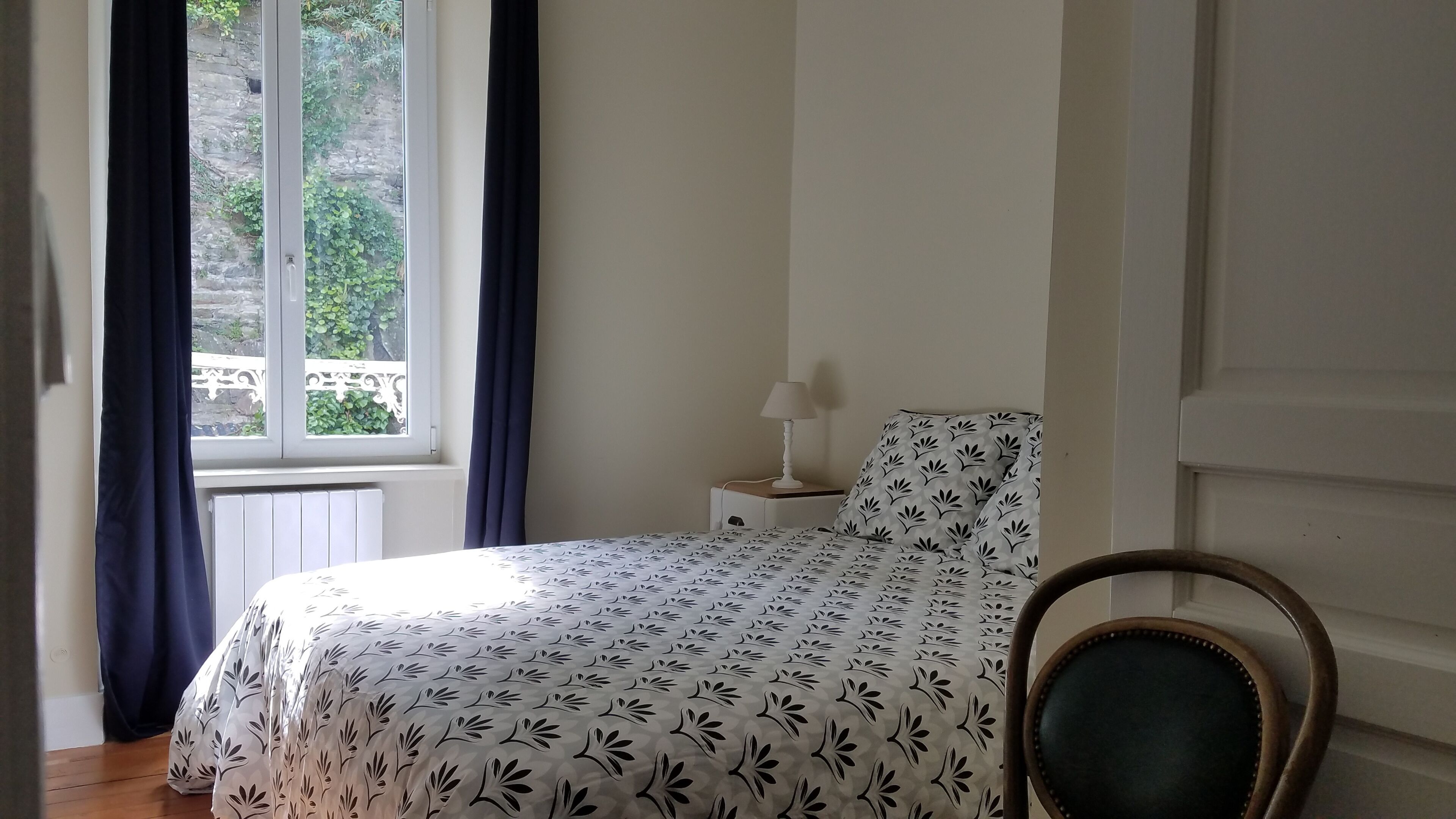 A bedroom with a bed, a nightstand, a lamp, and a chair.