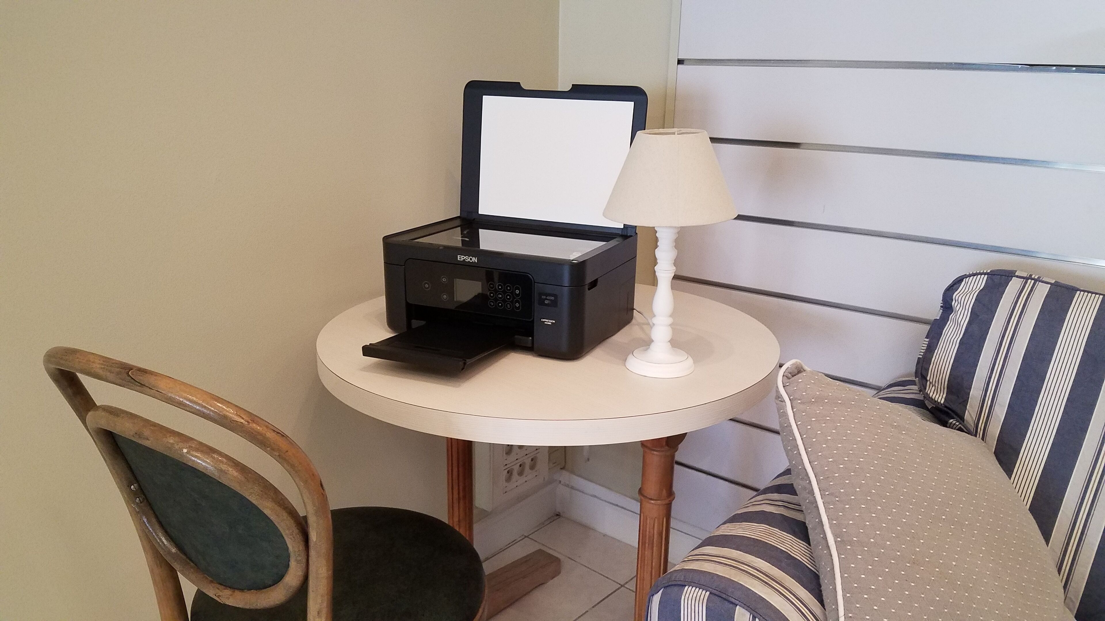 Una mesa pequeña y redonda con una impresora, una lámpara y una silla.