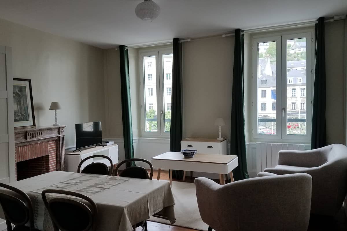 A room with a dining table, chairs, a TV, a small cabinet, and a window with curtains.