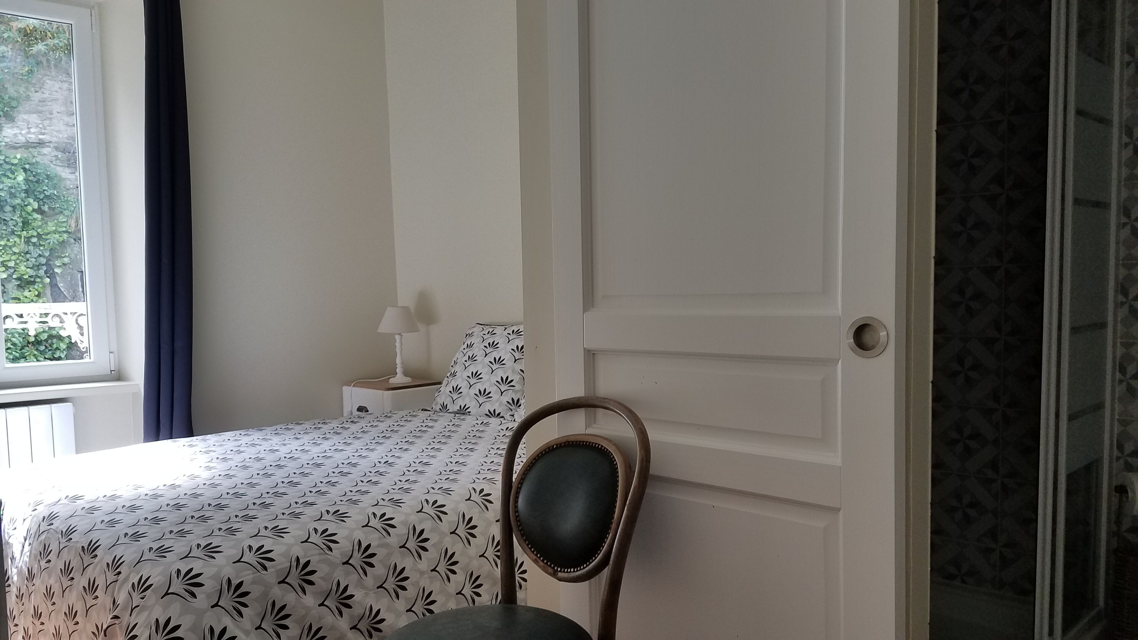 A bedroom with a bed, a nightstand, a chair, and a window with curtains.