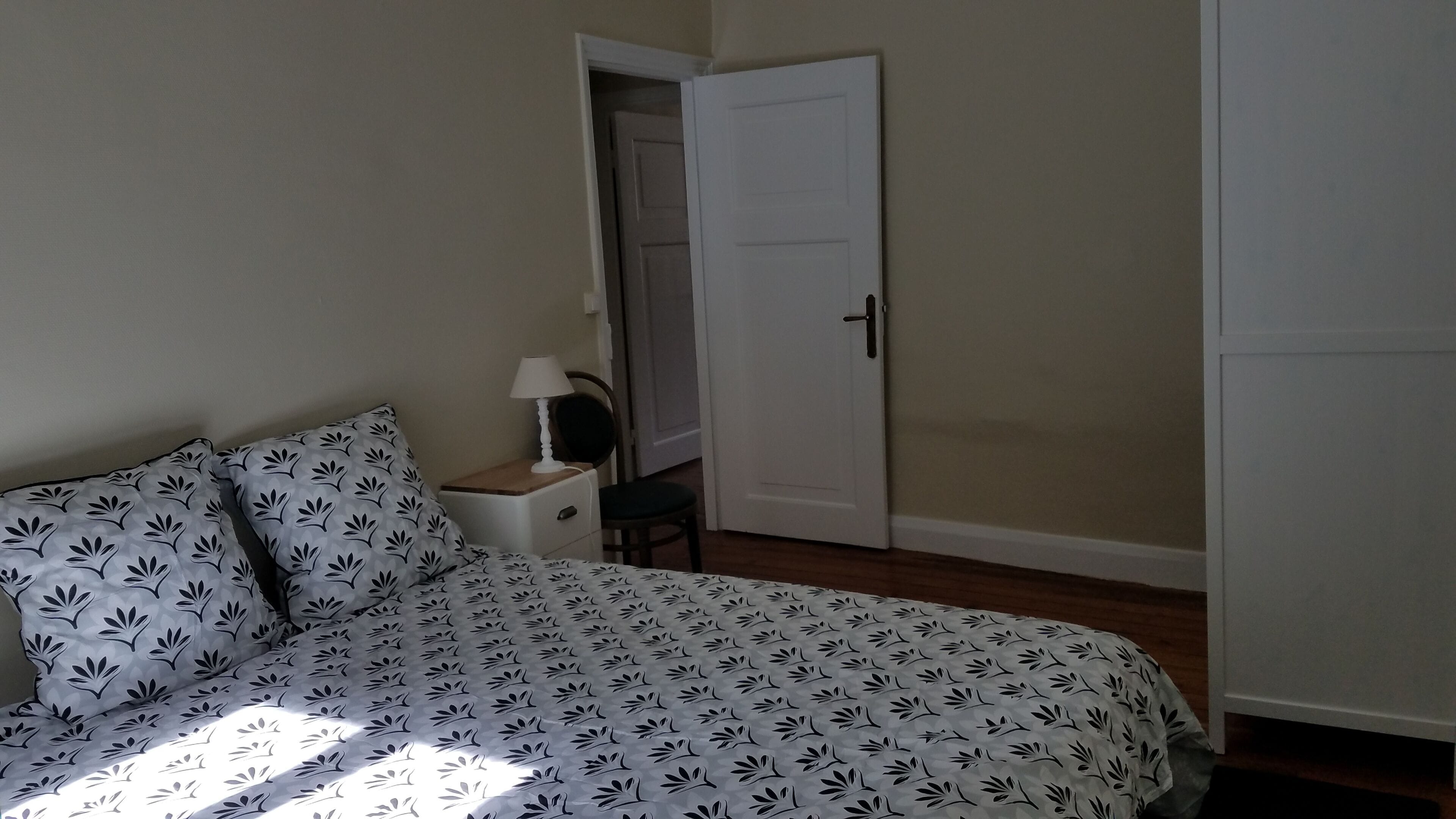 Un dormitorio con cama, mesita de noche, silla y puerta.