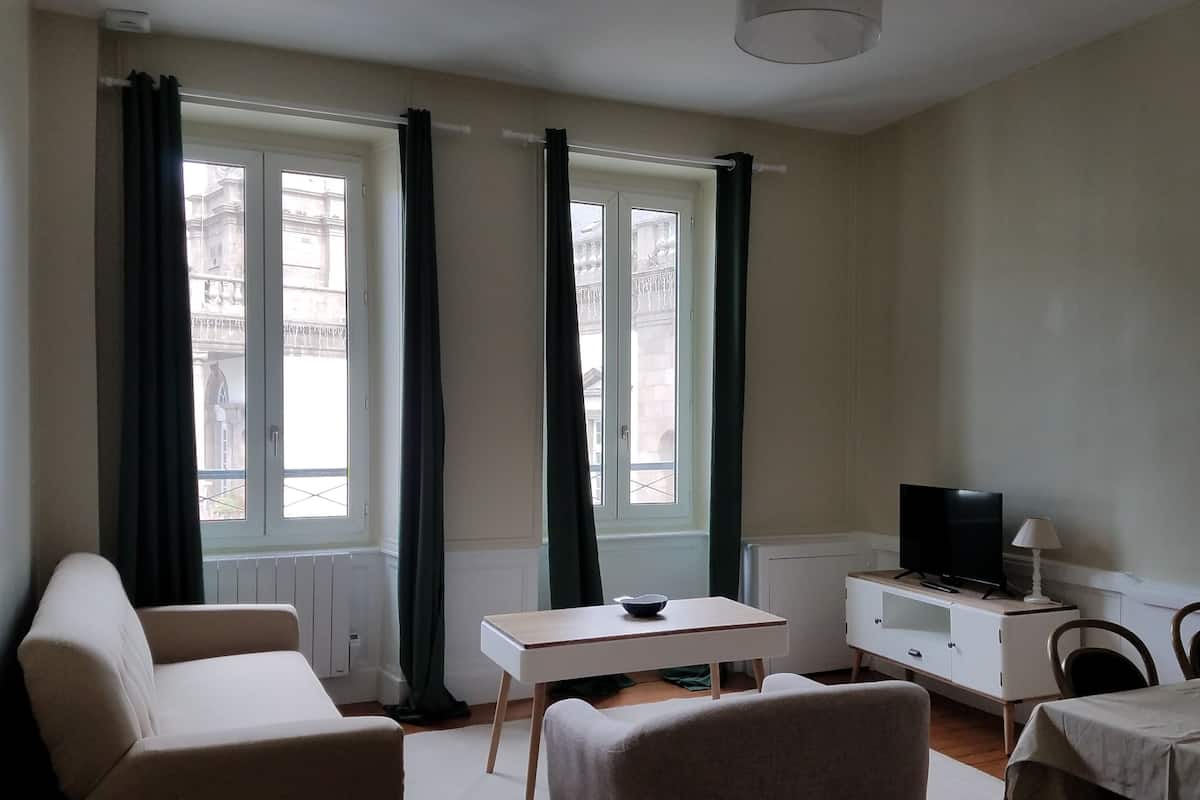 A small, well-lit room with a sofa, a table, a TV, and a lamp.