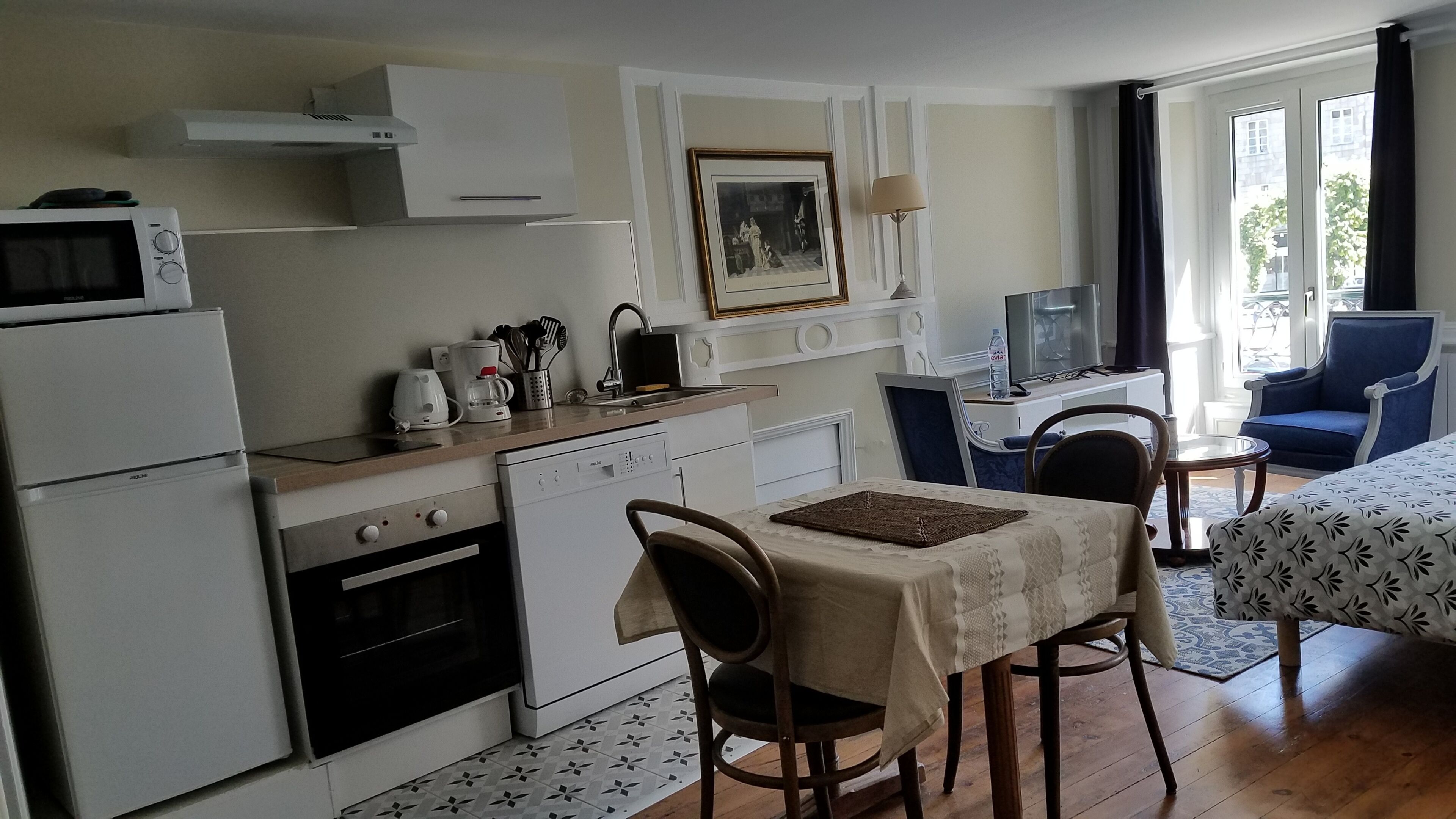 A compact kitchen with a microwave, coffee maker, and sink. There is a dining area with a table and chairs, and a TV in the corner.