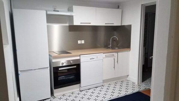 A compact kitchen with white cabinets, a dishwasher, an oven, and a sink. - Appart'hotel de la Mairie (Morlaix)