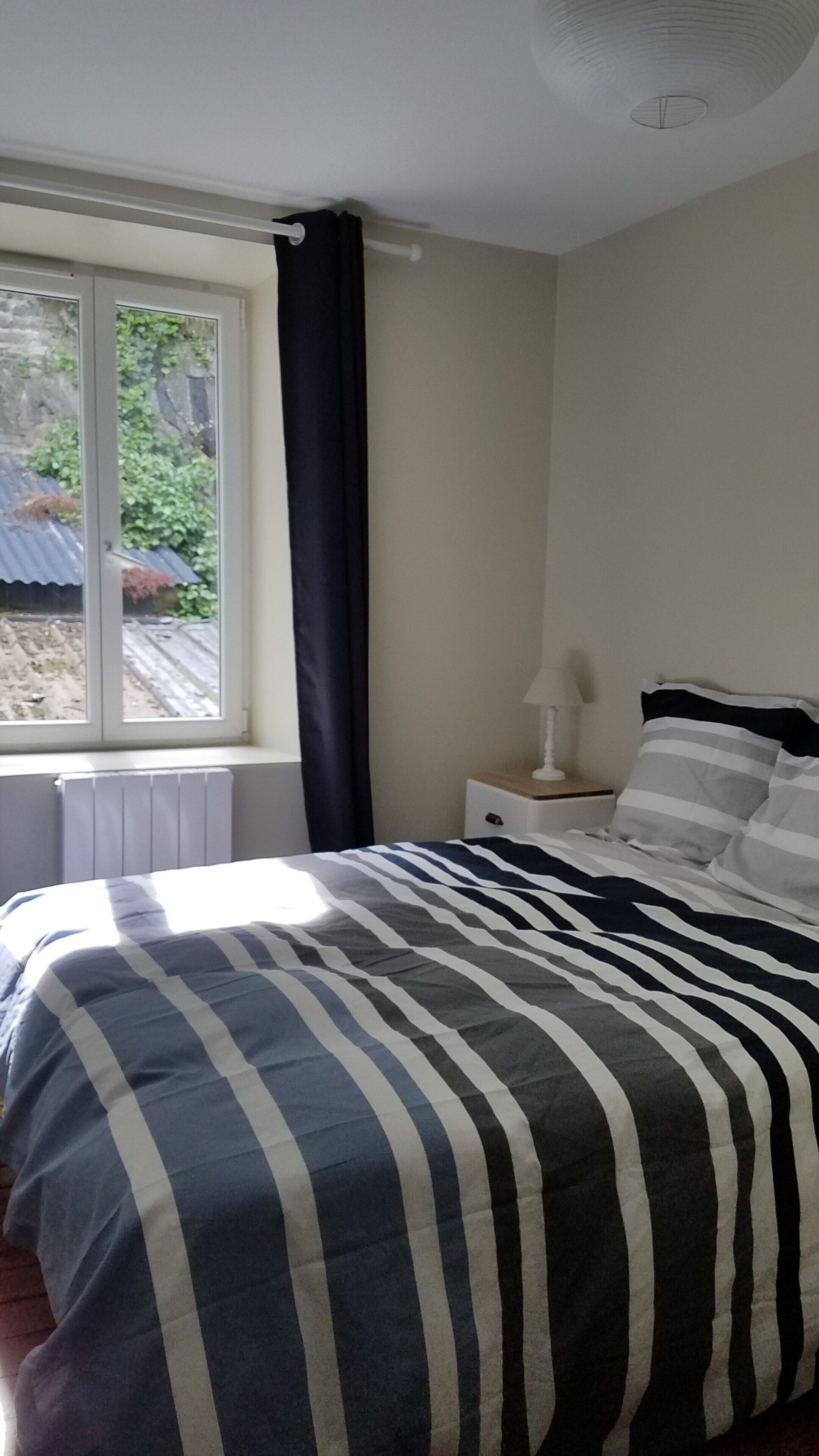 Un dormitorio con una cama, una ventana, un radiador y una mesita de noche con una lámpara.