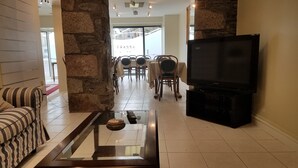 Uma sala de estar com sofá, mesa de centro de vidro, televisão e parede de pedra.