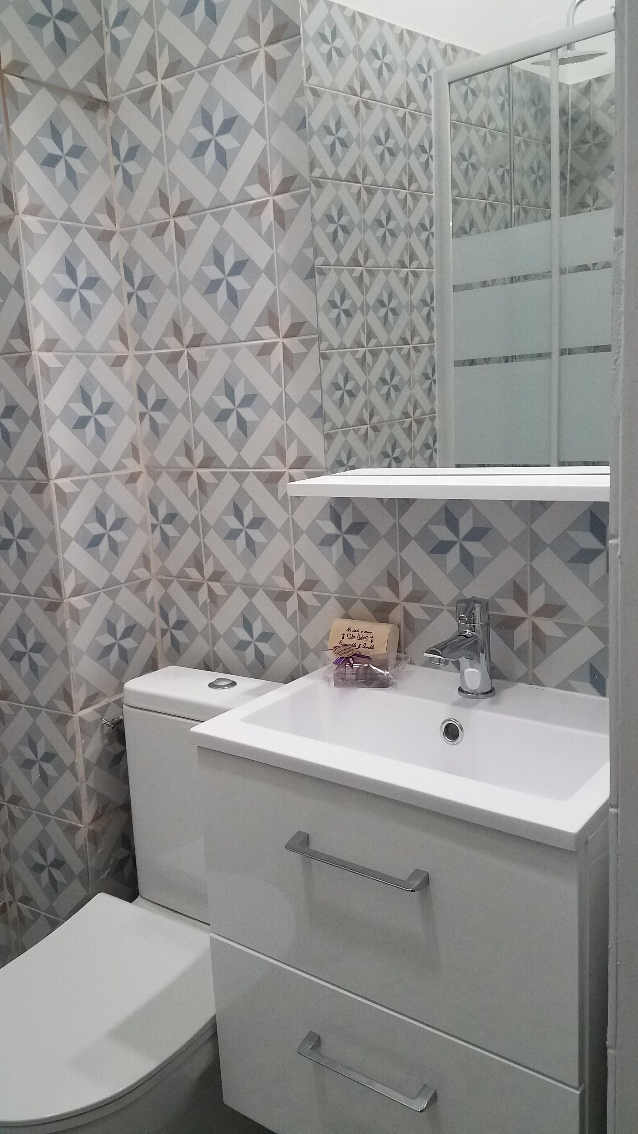 A bathroom with a white toilet, a sink with a mirror above it, and patterned tiles on the walls.