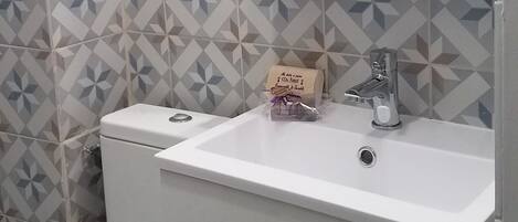 A bathroom with a white toilet, a sink with a mirror above it, and patterned tiles on the walls.