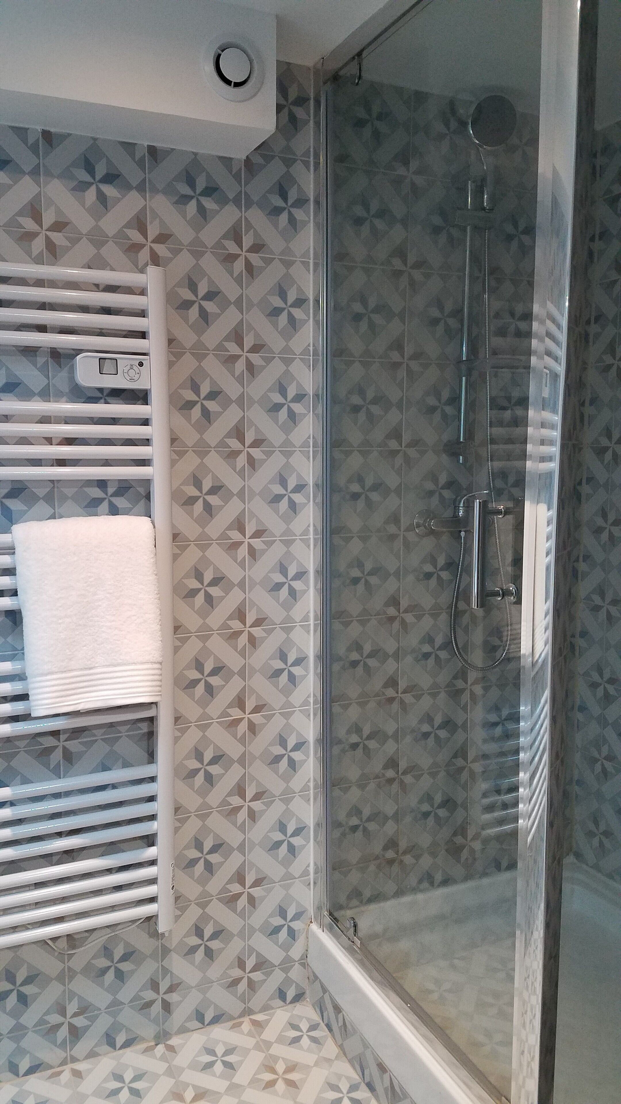 Un baño con ducha, azulejos decorados, un perchero y un panel de control.