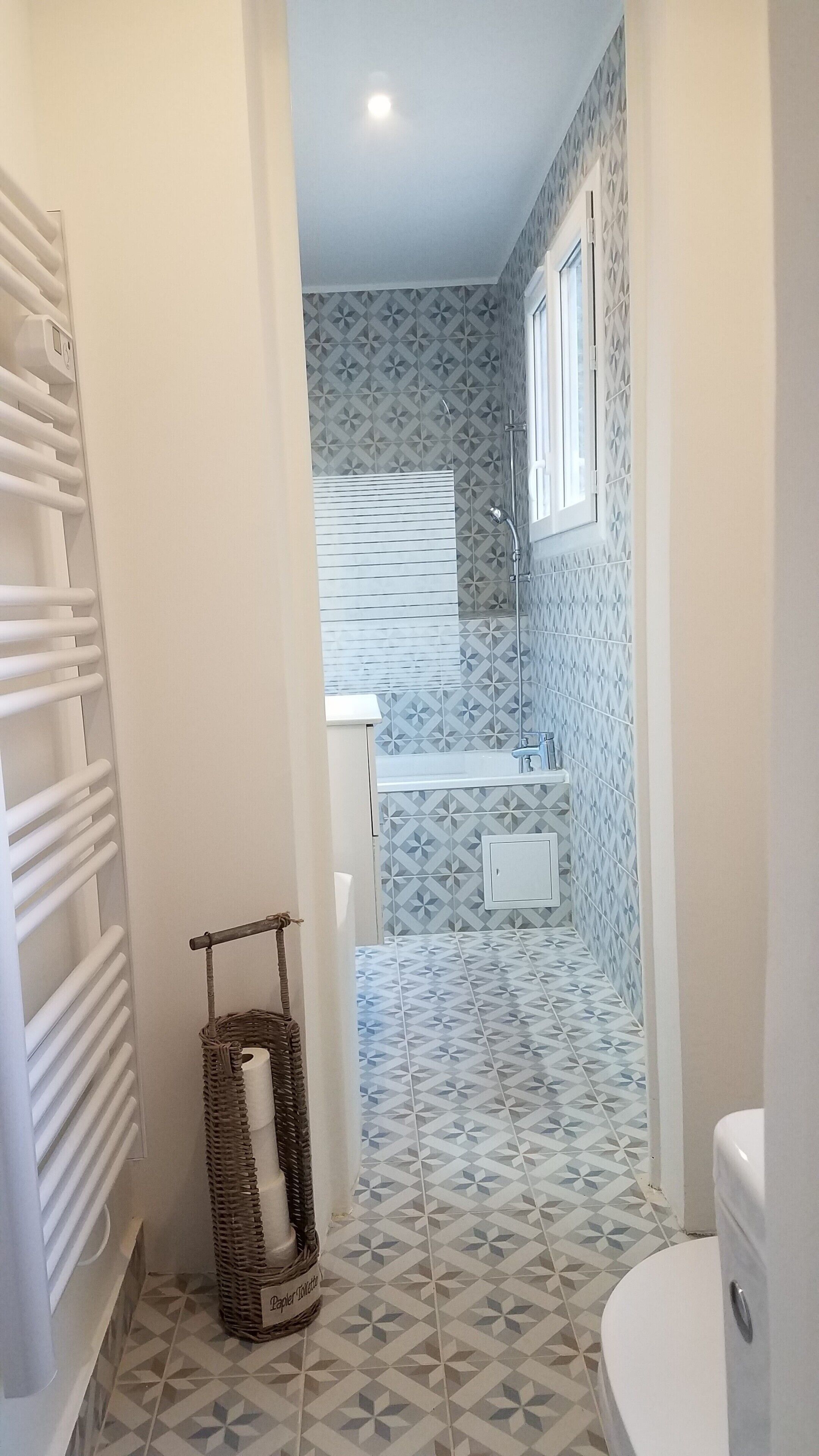 Un baño con baldosas estampadas, inodoro blanco, ducha y toallero.