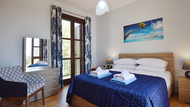 Un dormitorio con cama, una silla, un escritorio, una ventana con cortinas y un cuadro en la pared.
