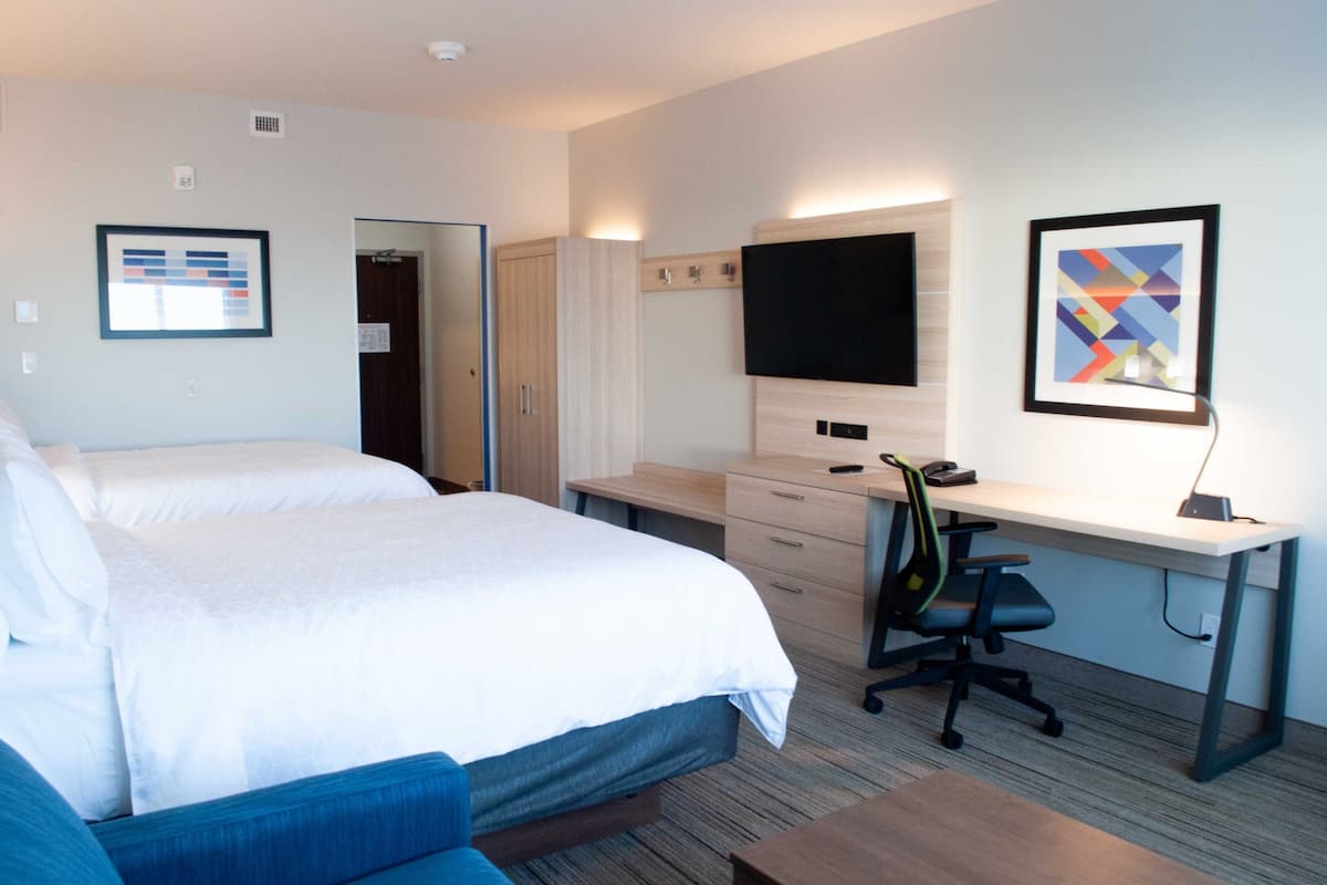 A hotel room with two beds, a desk, a chair, a TV, and artwork on the walls.