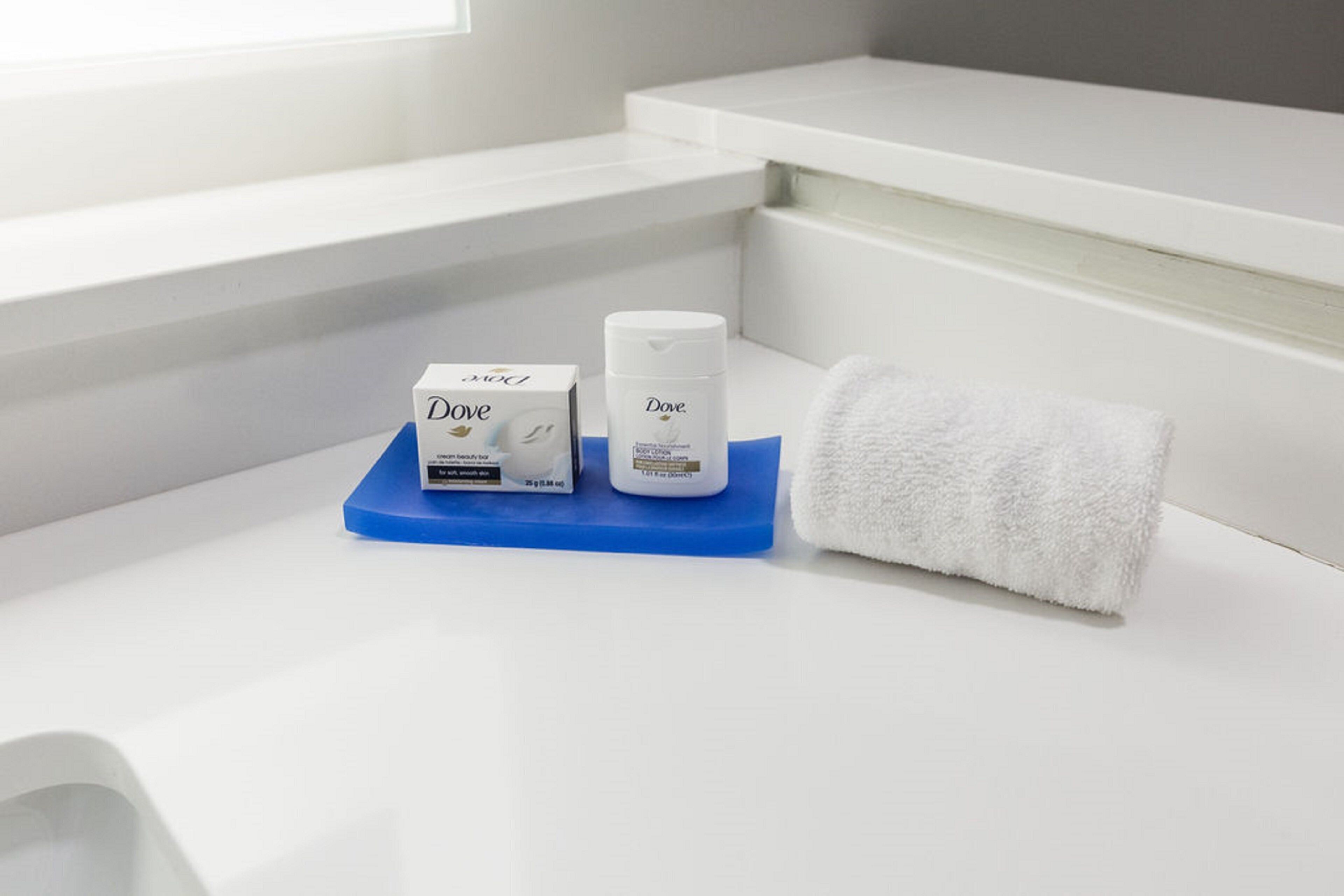 A bathroom with a white sink, a blue soap dish, Dove soap, and a white towel.