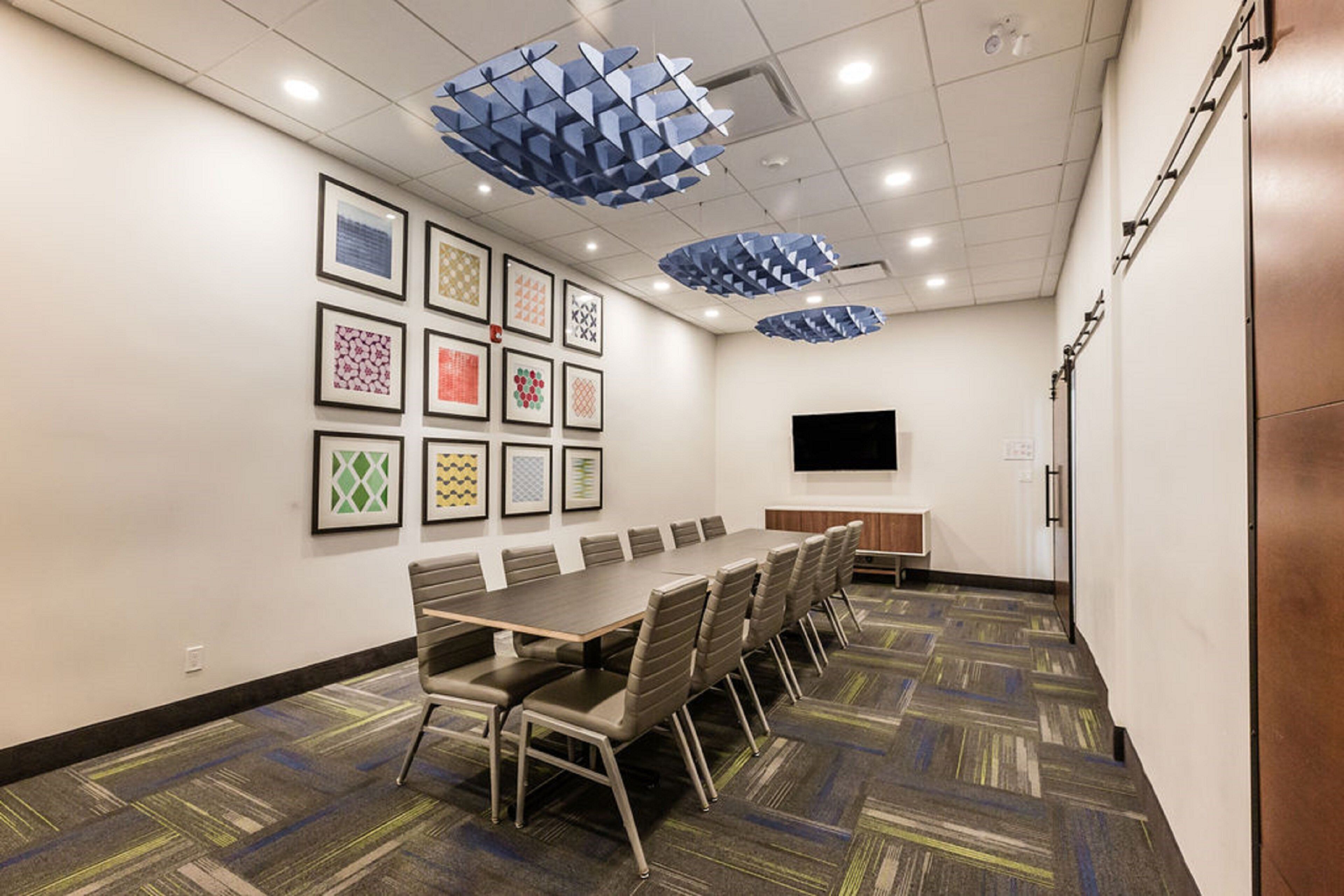 A conference room with a long table, chairs, framed artwork on the walls, and a flat-screen TV.