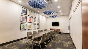 A conference room with a long table, chairs, framed artwork on the walls, and a flat-screen TV.