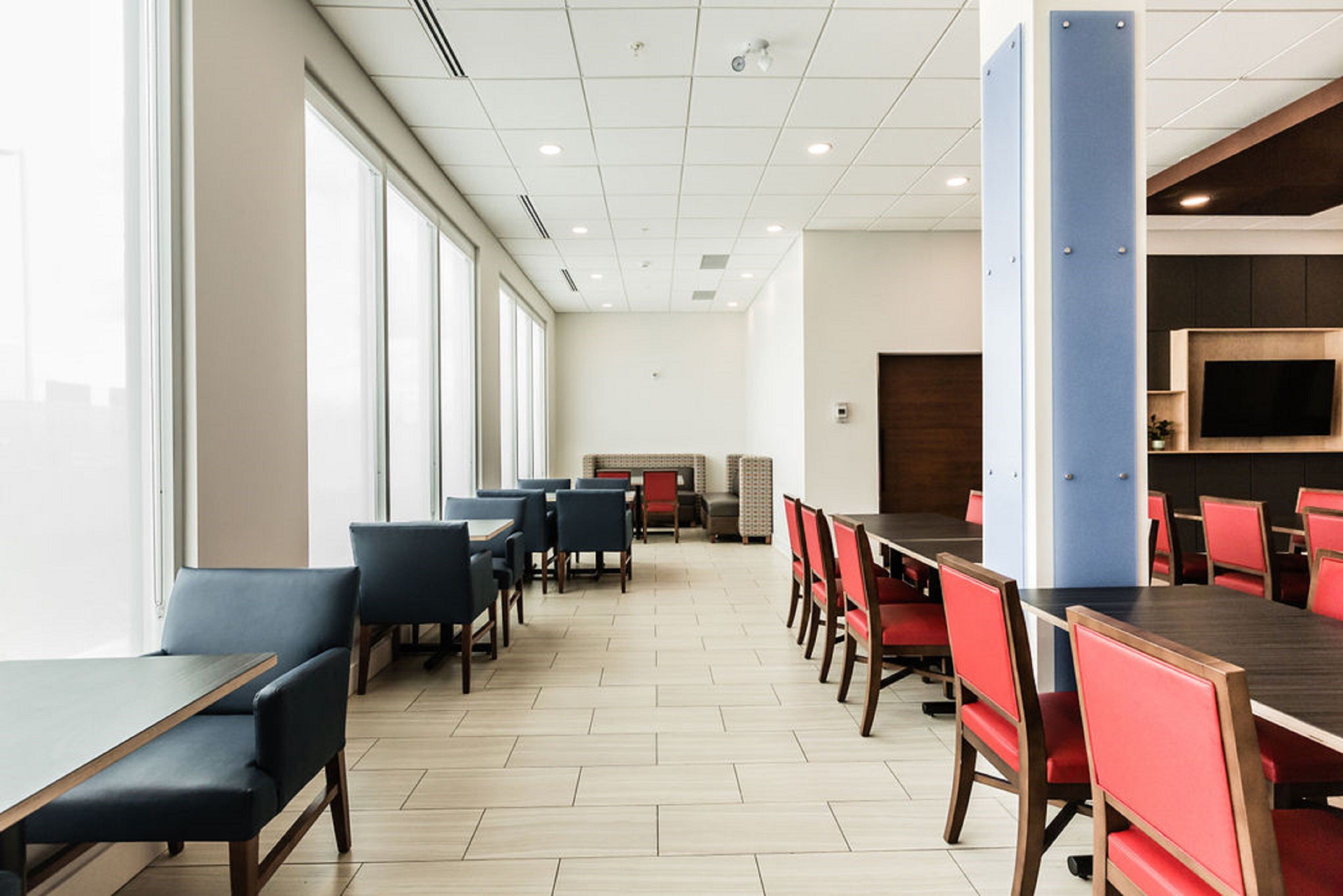 A spacious dining area with long tables and chairs, large windows, and a modern ceiling design.