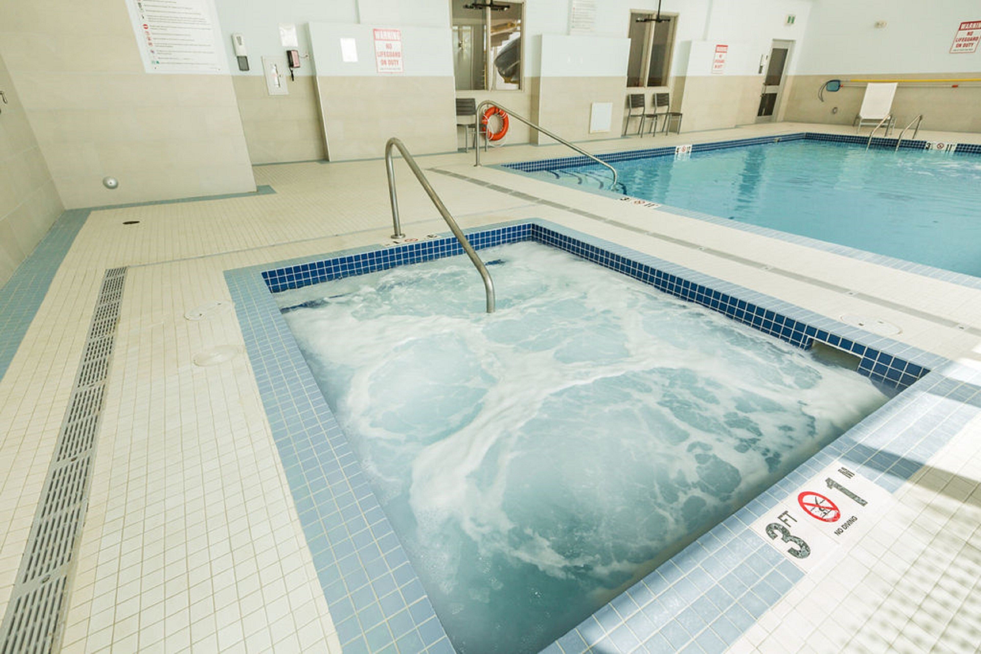 A swimming pool with a hot tub area, tiled flooring, and safety signs.