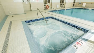 A swimming pool with a hot tub area, tiled flooring, and safety signs.