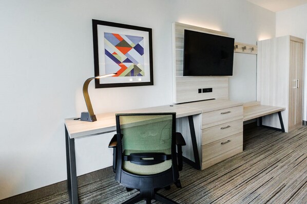 Habitación de hotel moderna con escritorio, silla, televisor y una obra de arte abstracta enmarcada en la pared.