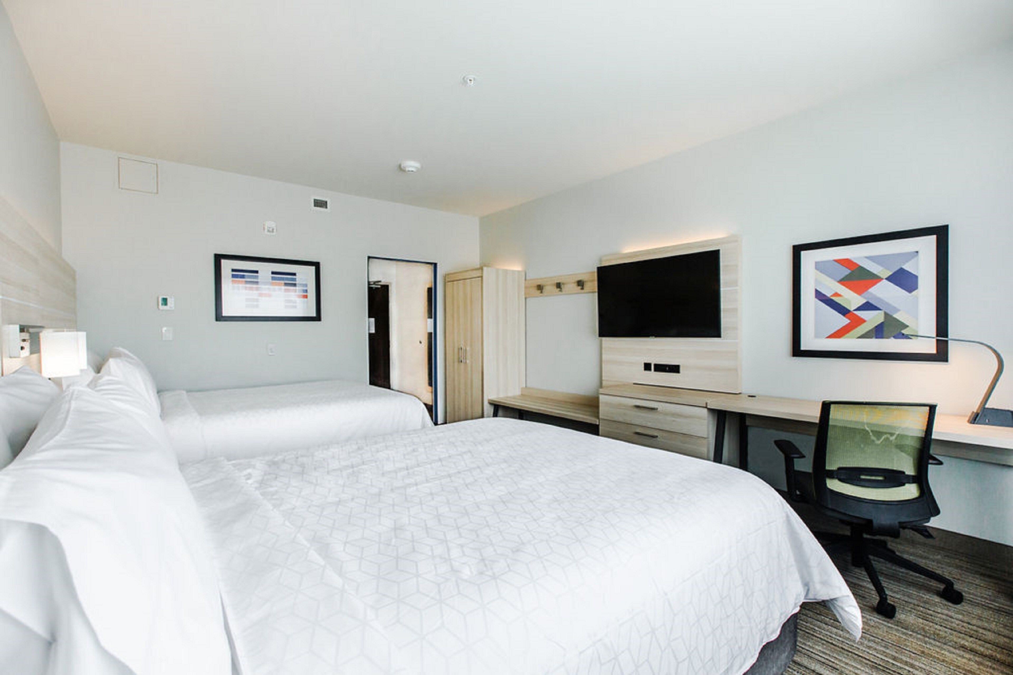A hotel room with two beds, a desk, a chair, a flat-screen TV, and a framed abstract painting.
