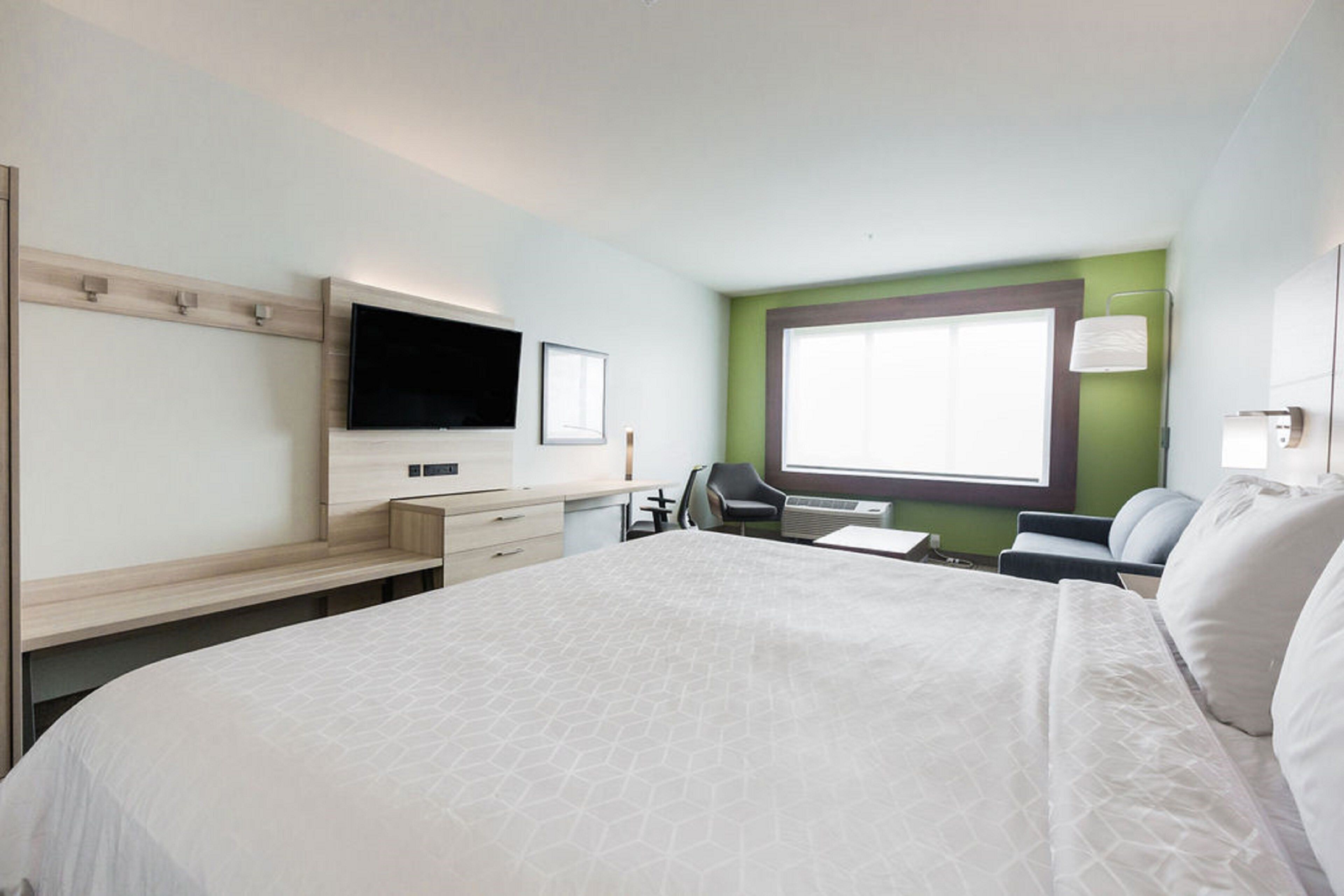 A hotel room with a large bed, a desk with a computer, a TV, and a window with a view.