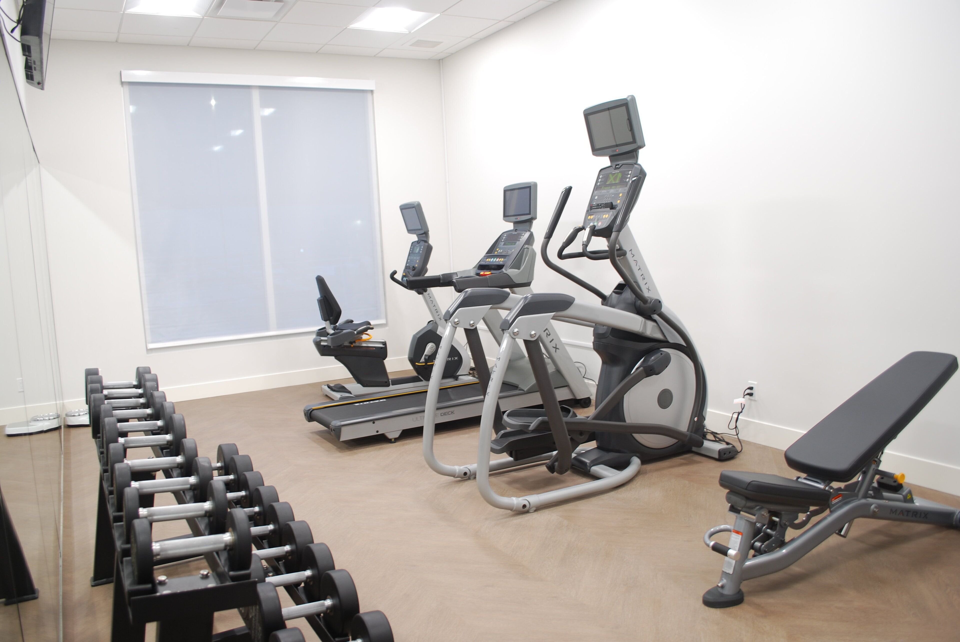 Une salle de sport équipée de tapis de course, d’un banc et d’haltères.