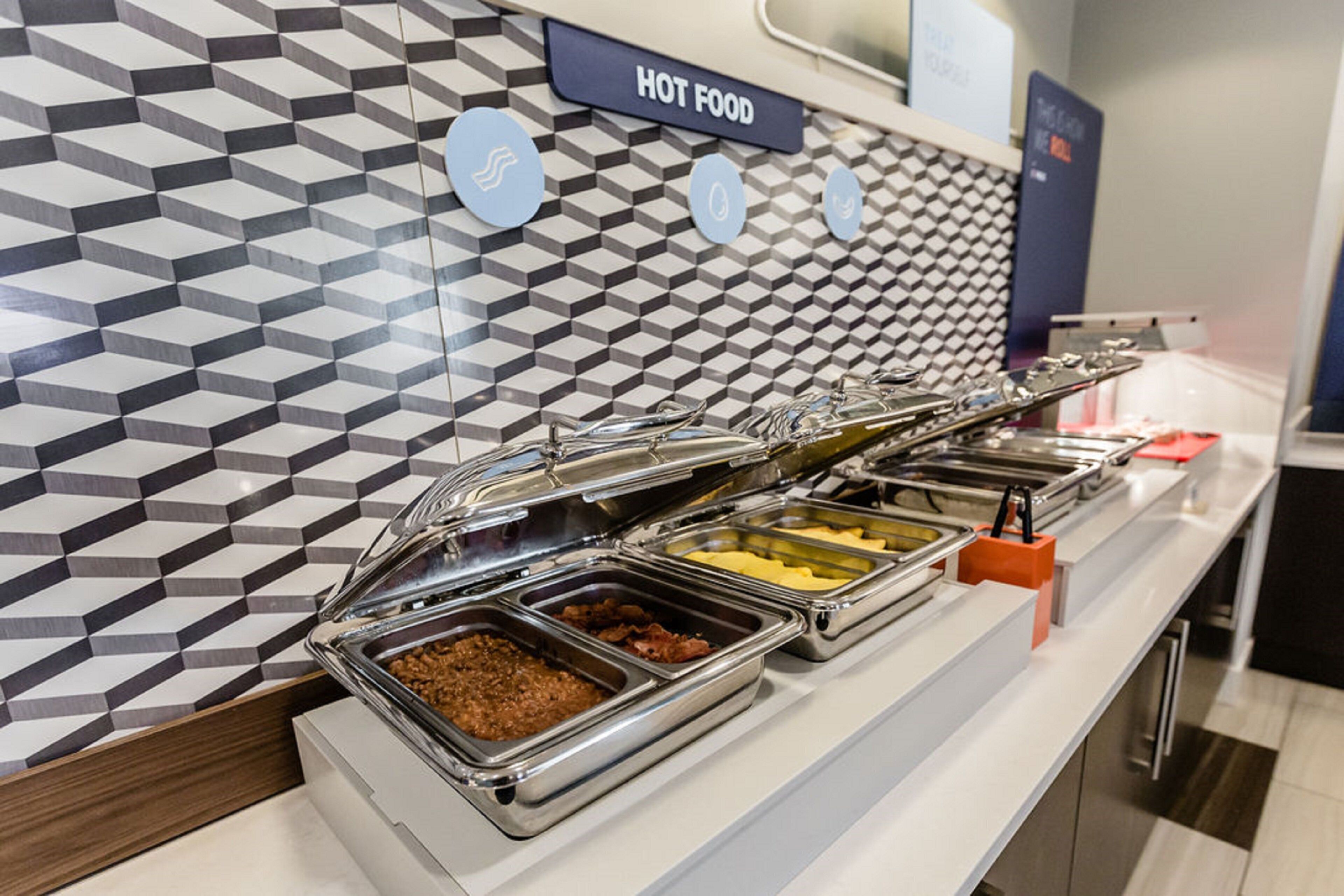 Ein Buffet mit verschiedenen Speisen, ein Schild mit der Aufschrift 'HEISSE SPEISEN' und eine strukturierte Wand im Hintergrund.