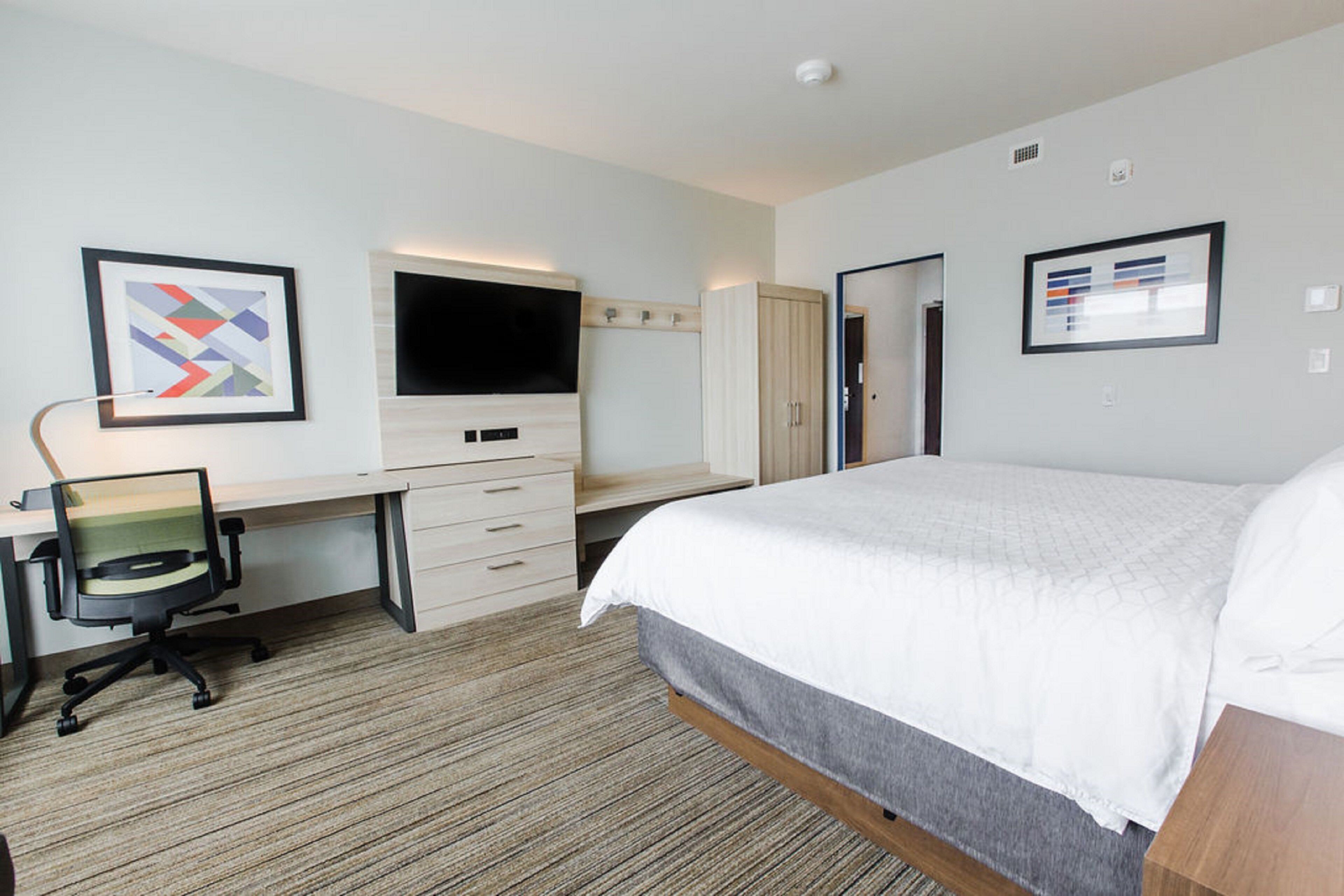 A hotel room with a bed, a desk with a chair, a television, and a wardrobe.