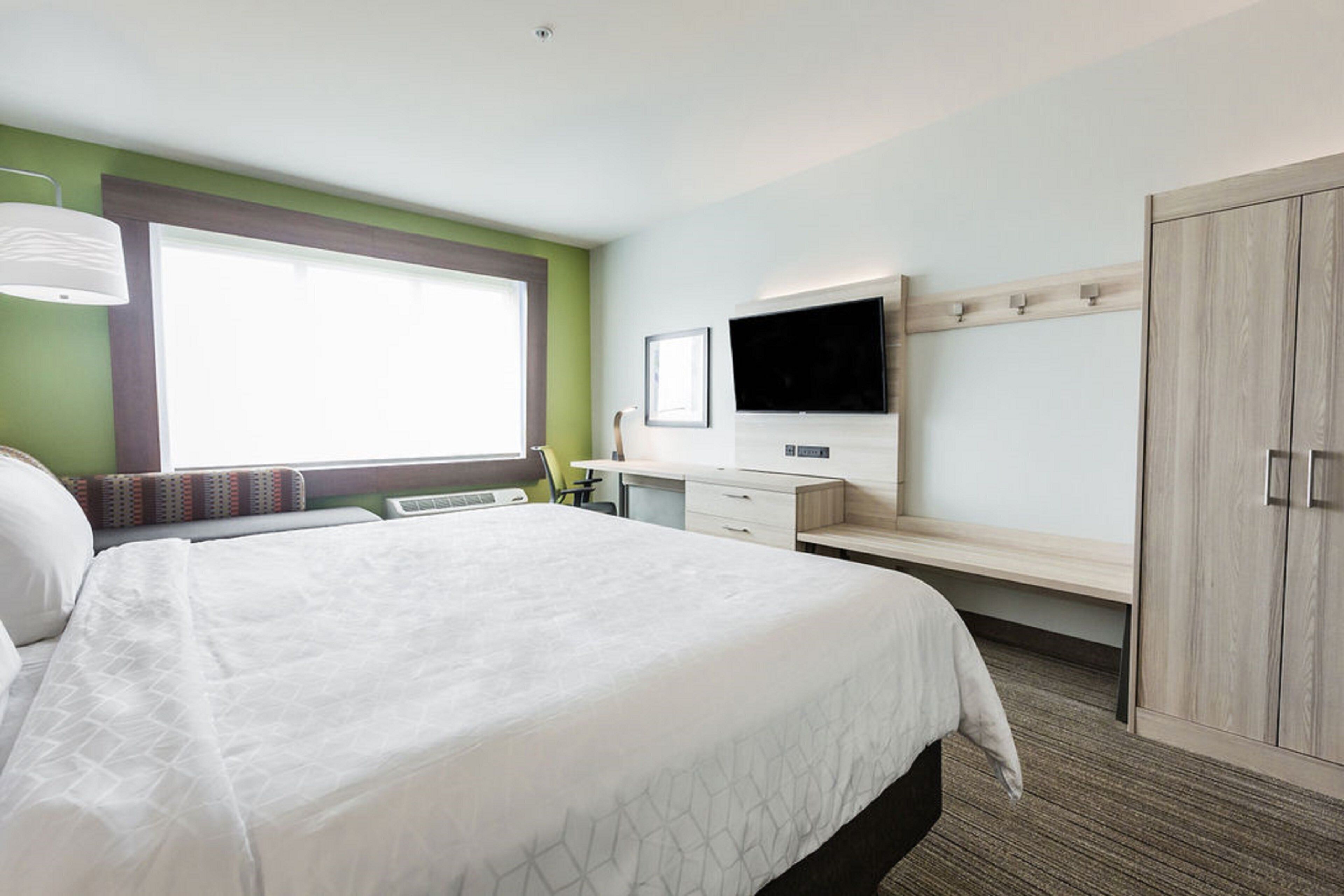 A hotel room with a large bed, a desk, a TV mounted on the wall, and a wardrobe.
