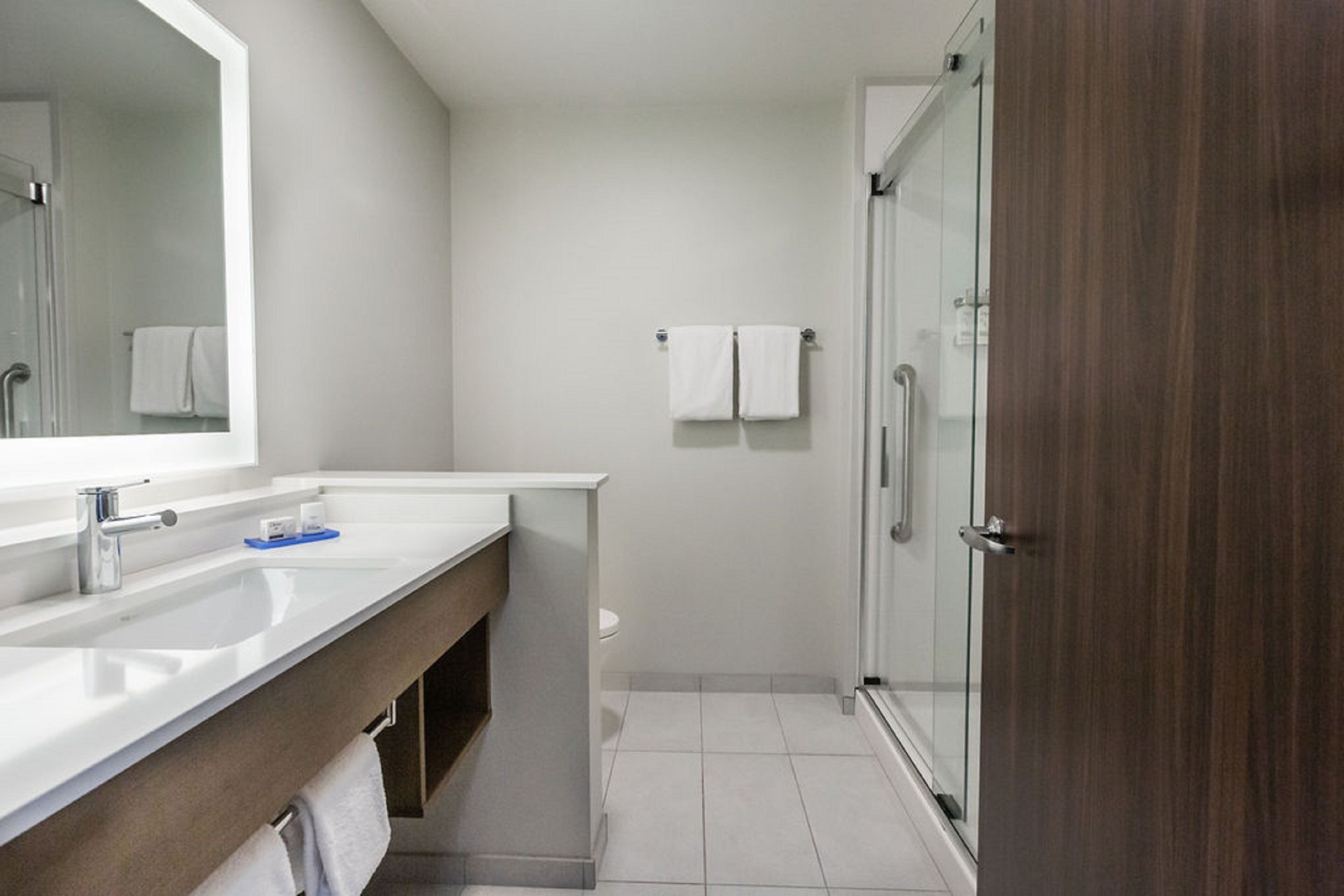 A modern bathroom with a large mirror, two sinks, a shower, and a toilet.