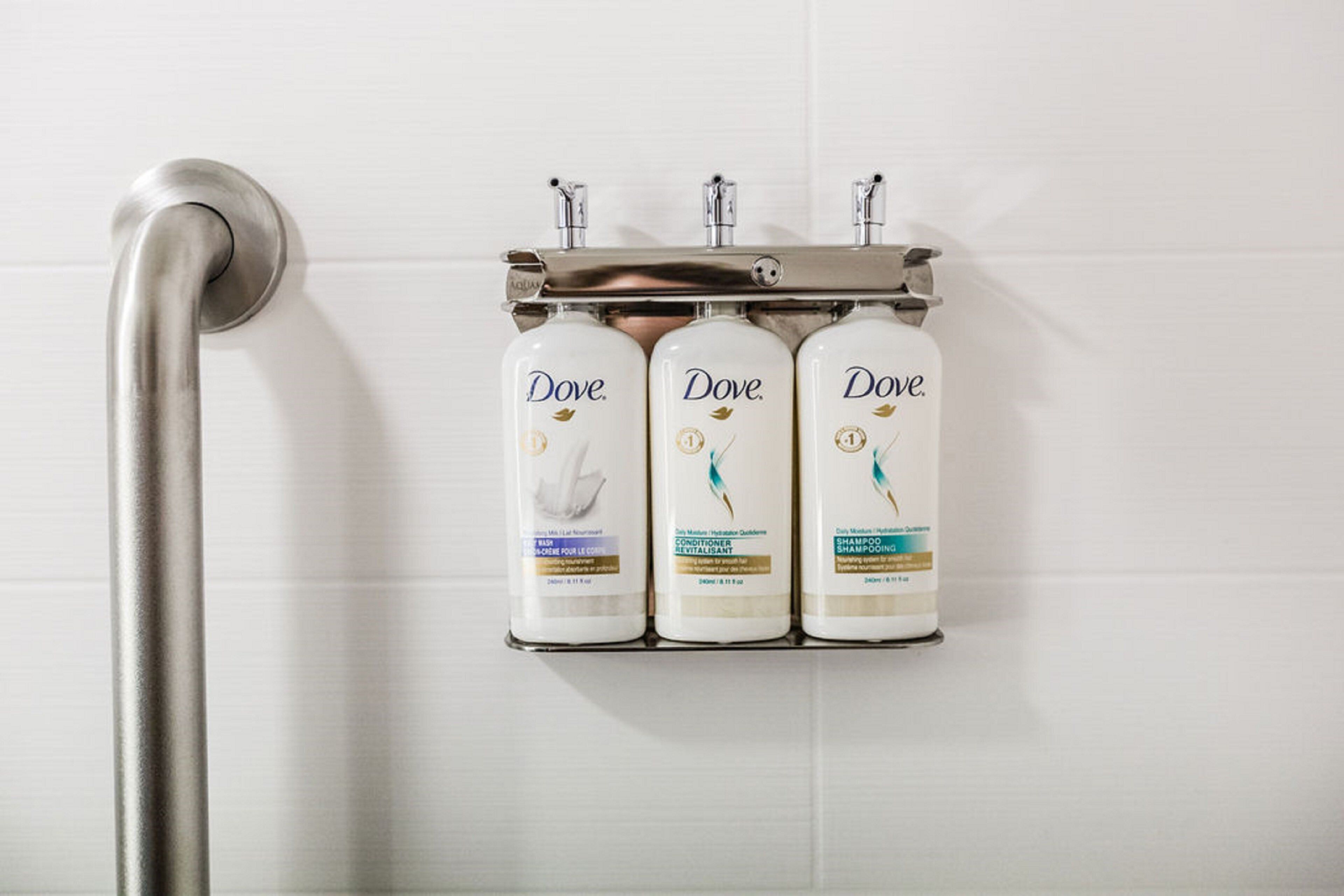 A shower area with a handrail and three Dove shampoo bottles mounted on the wall.
