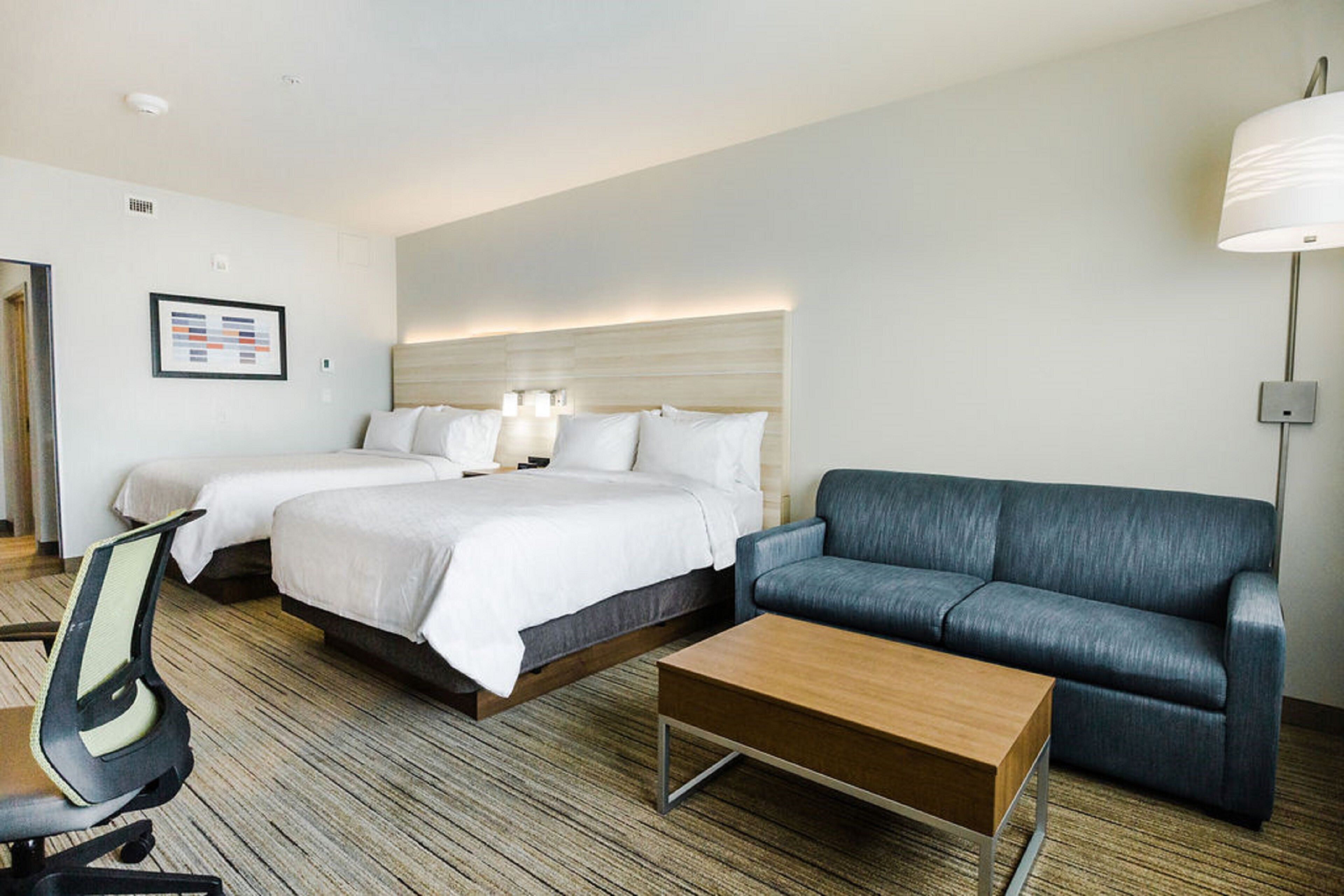 A hotel room with a bed, two bedside tables, a desk with a chair, a sofa, and a lamp.