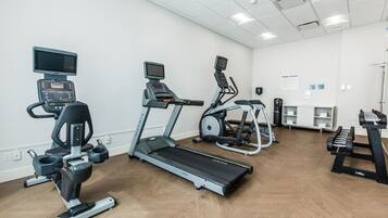 Ein Fitnessstudio mit Laufbändern, Crosstrainern und einer Gewichtshalterung.
