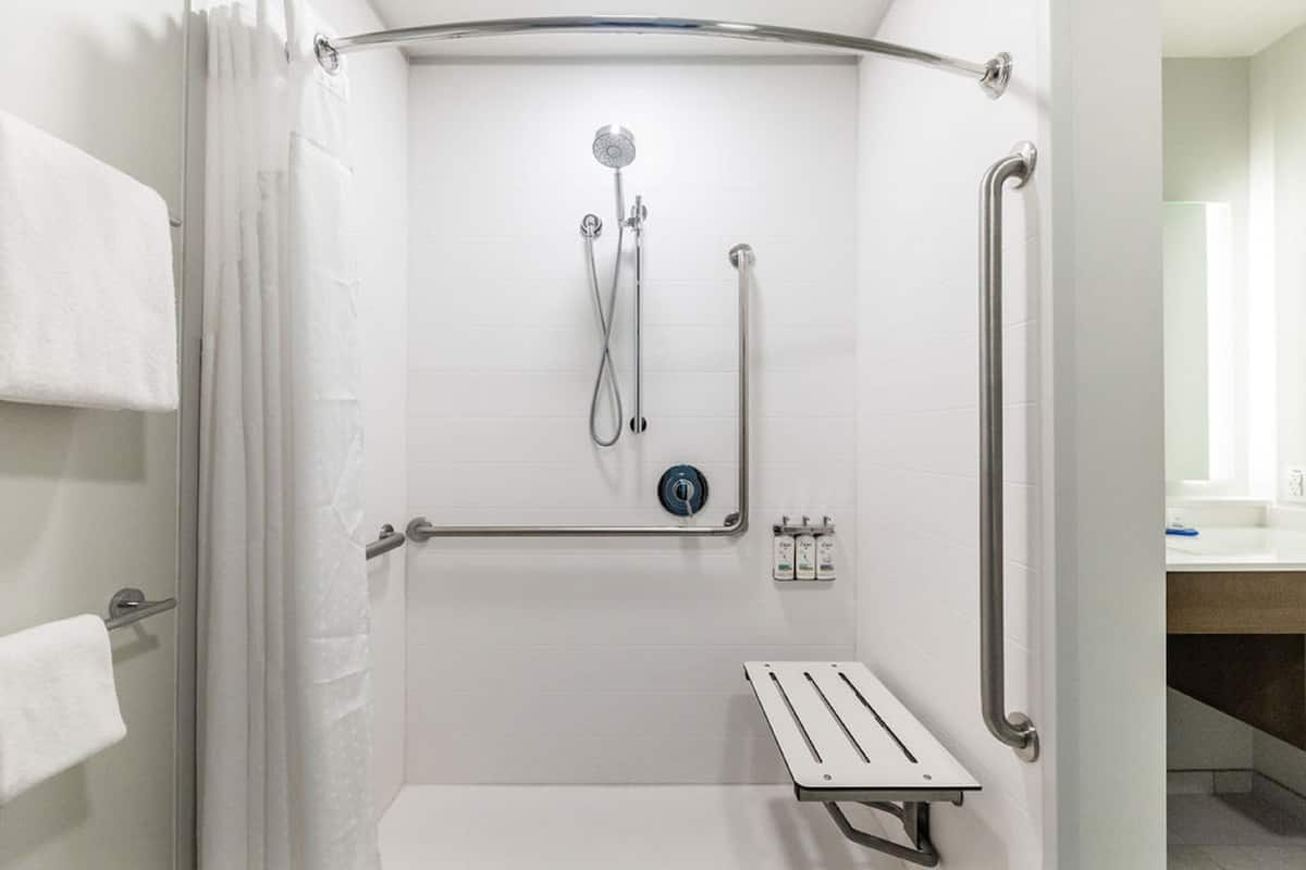 A shower area with a grab bar, a handheld showerhead, and a control panel.