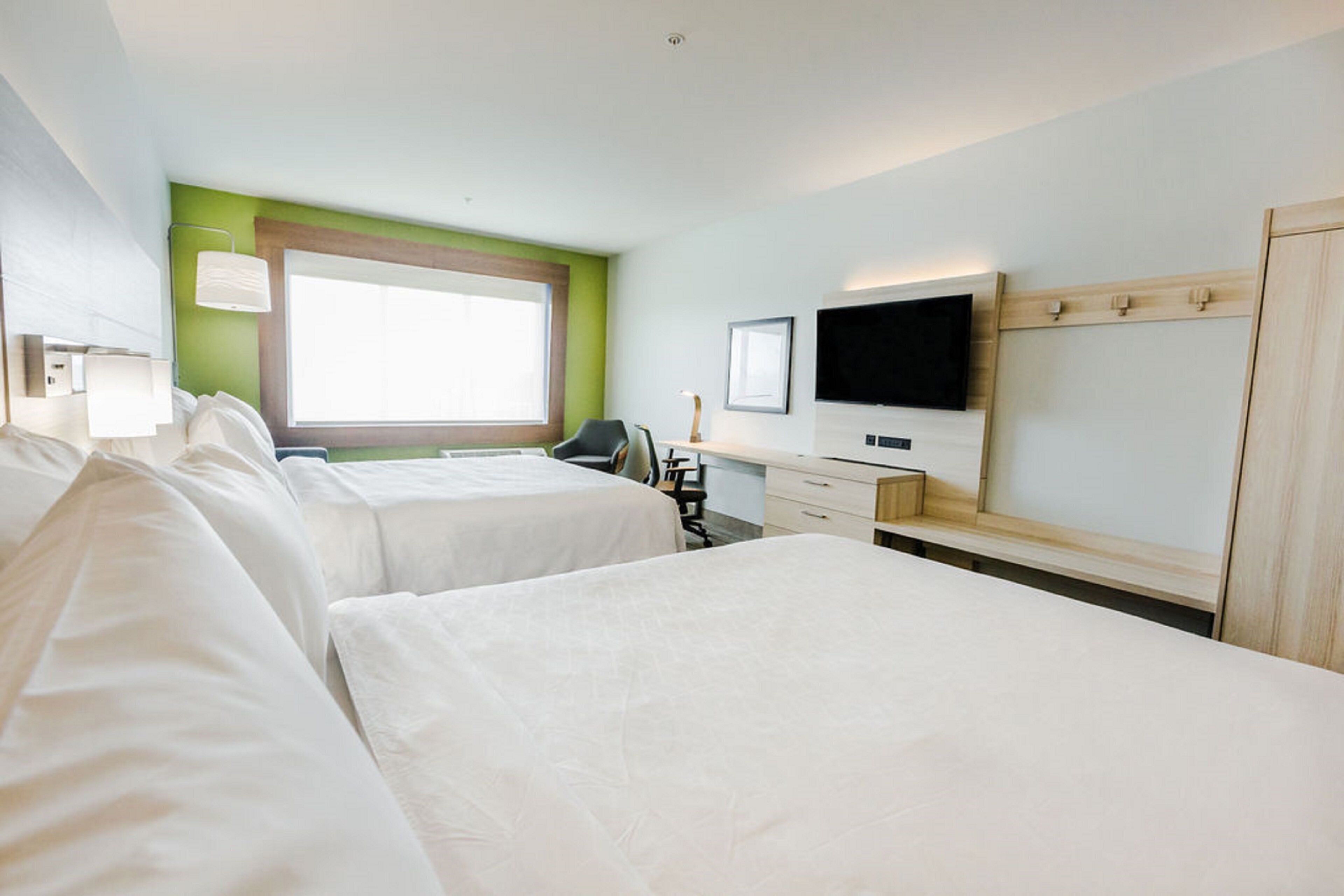 A hotel room with two beds, a desk, a chair, a television, and a window.