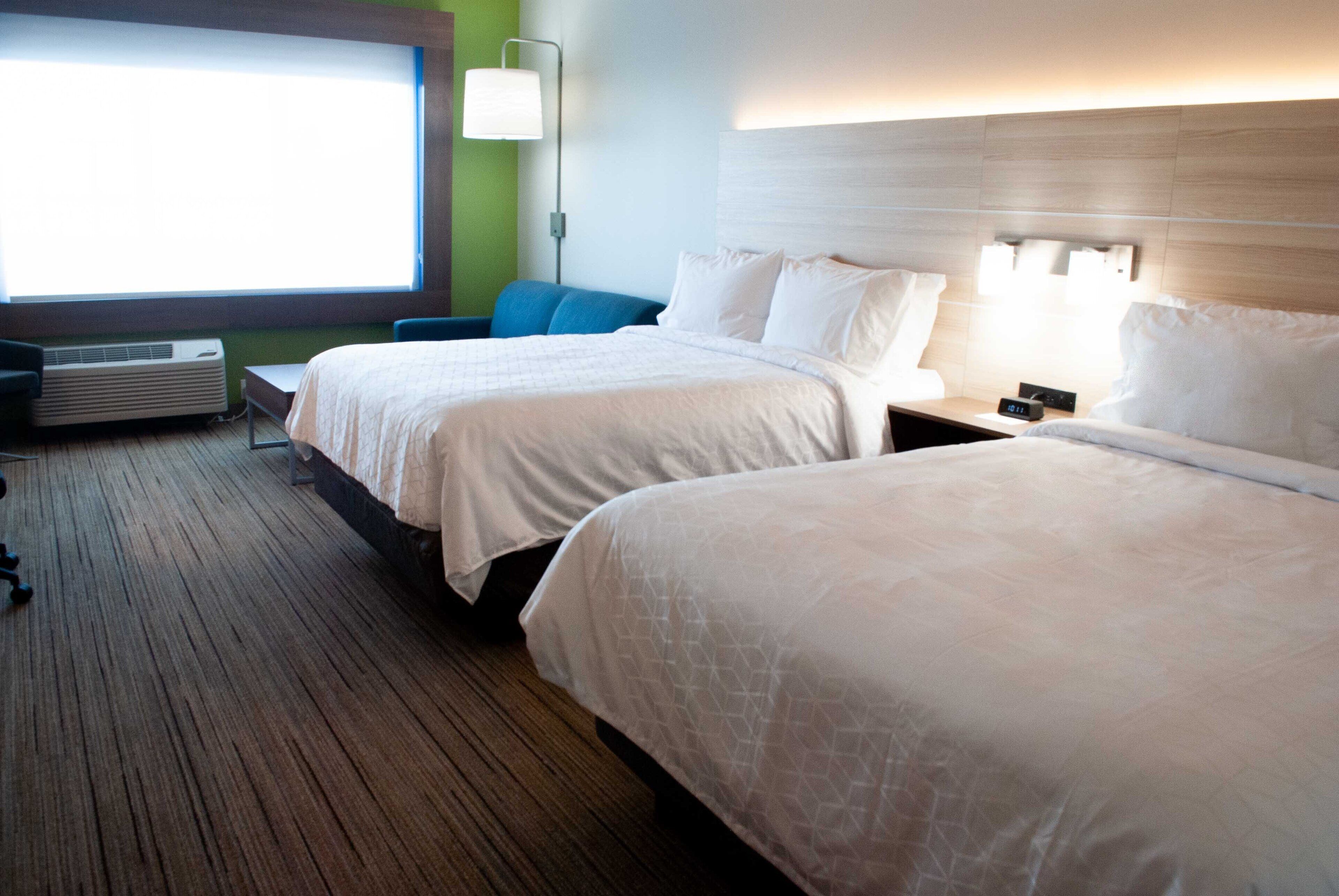 Une chambre d’hôtel avec deux lits, une grande fenêtre, un climatiseur, un bureau et une lampe.