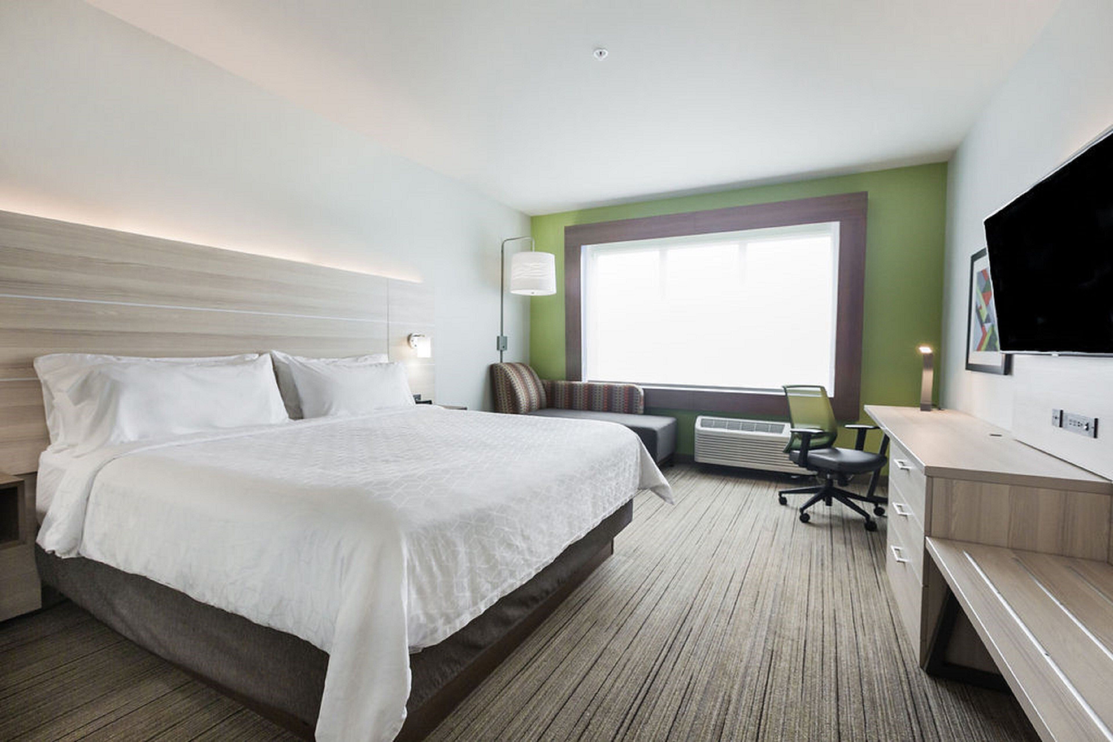 A hotel room with a large bed, a desk, a chair, and a television.