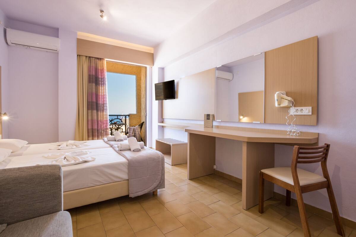 A hotel room with a bed, a desk, a chair, a TV, and a mirror.