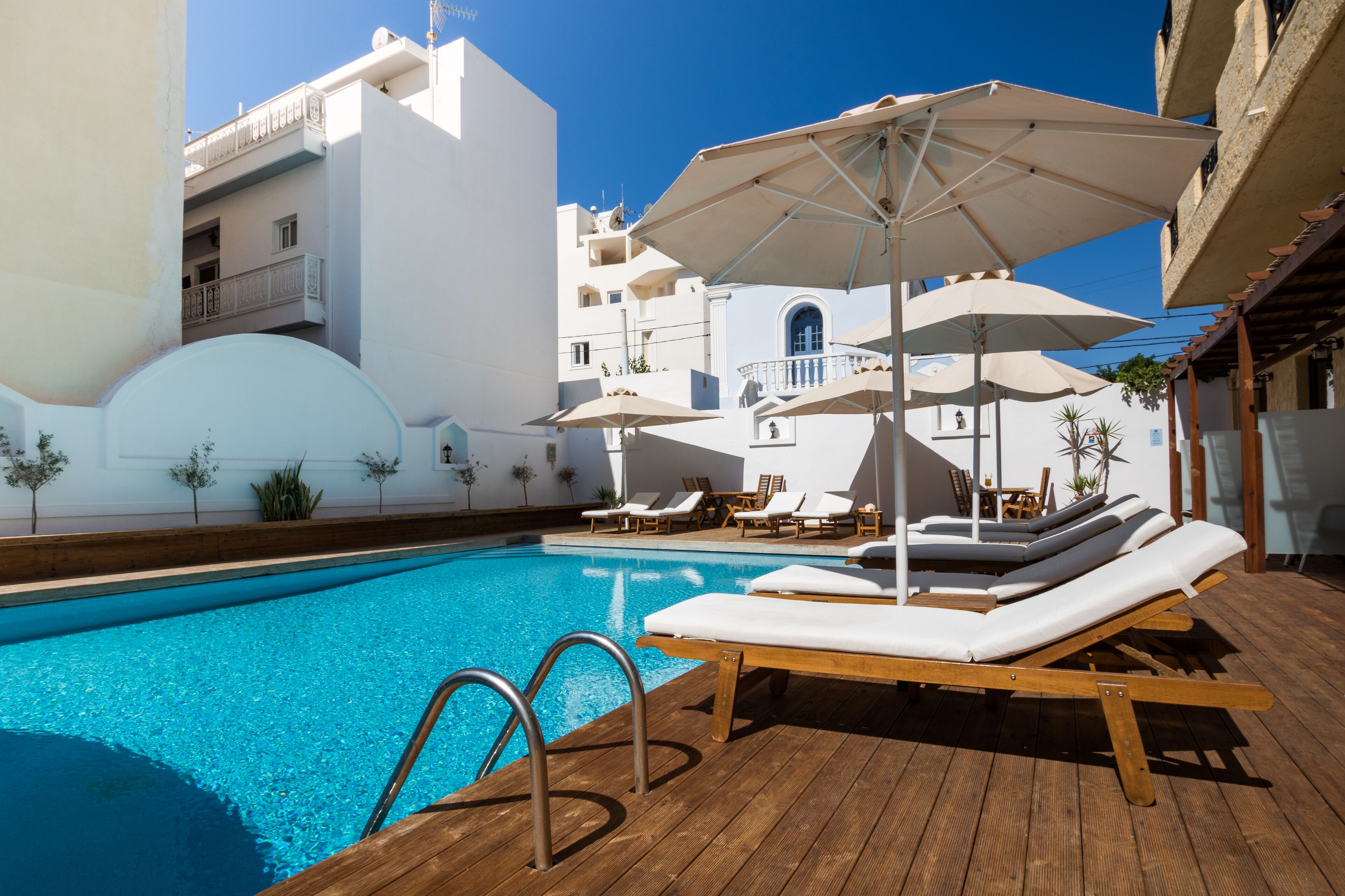 A swimming pool with lounge chairs and umbrellas, surrounded by white buildings with balconies.