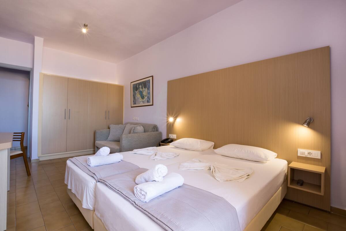 A hotel room with a large bed, a desk, a wardrobe, and a painting on the wall.