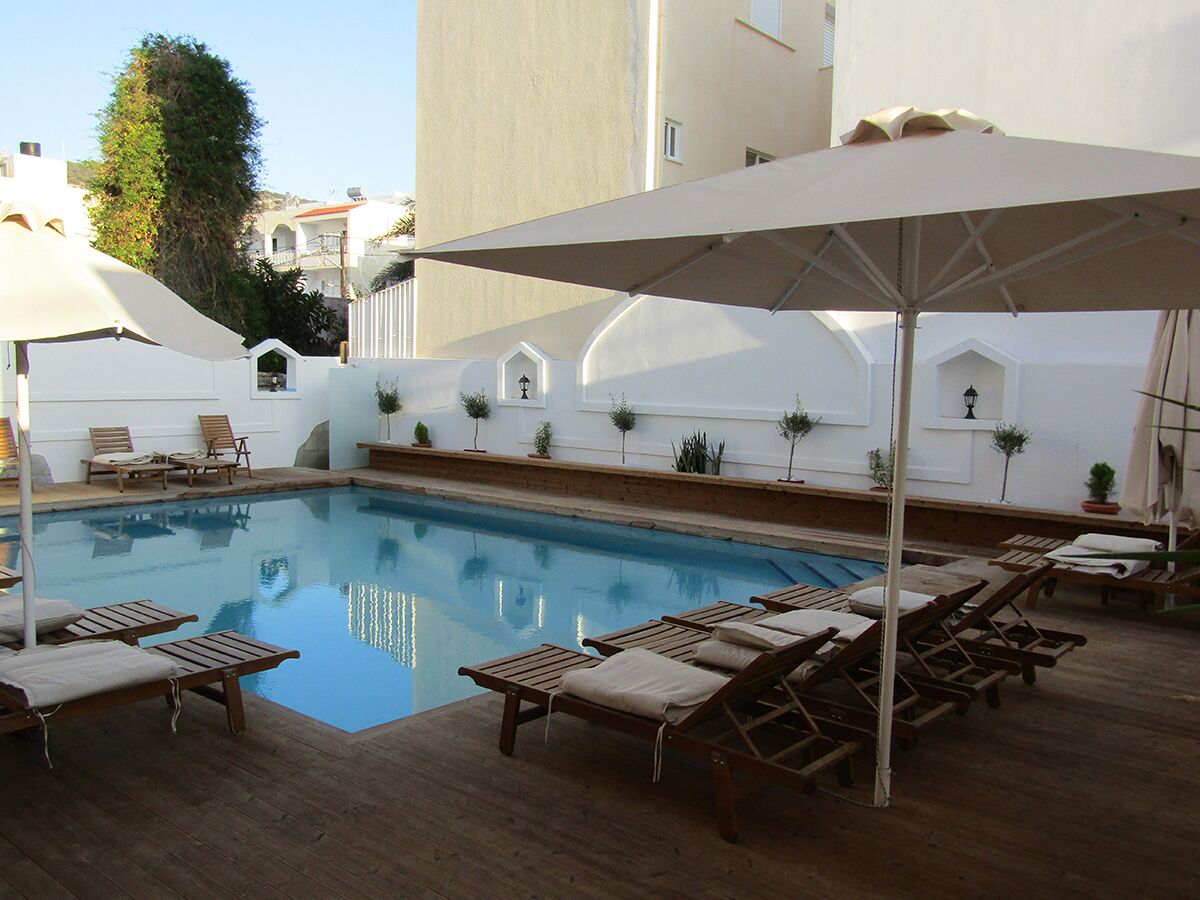 A pool area with lounge chairs and umbrellas, surrounded by white walls and potted plants.