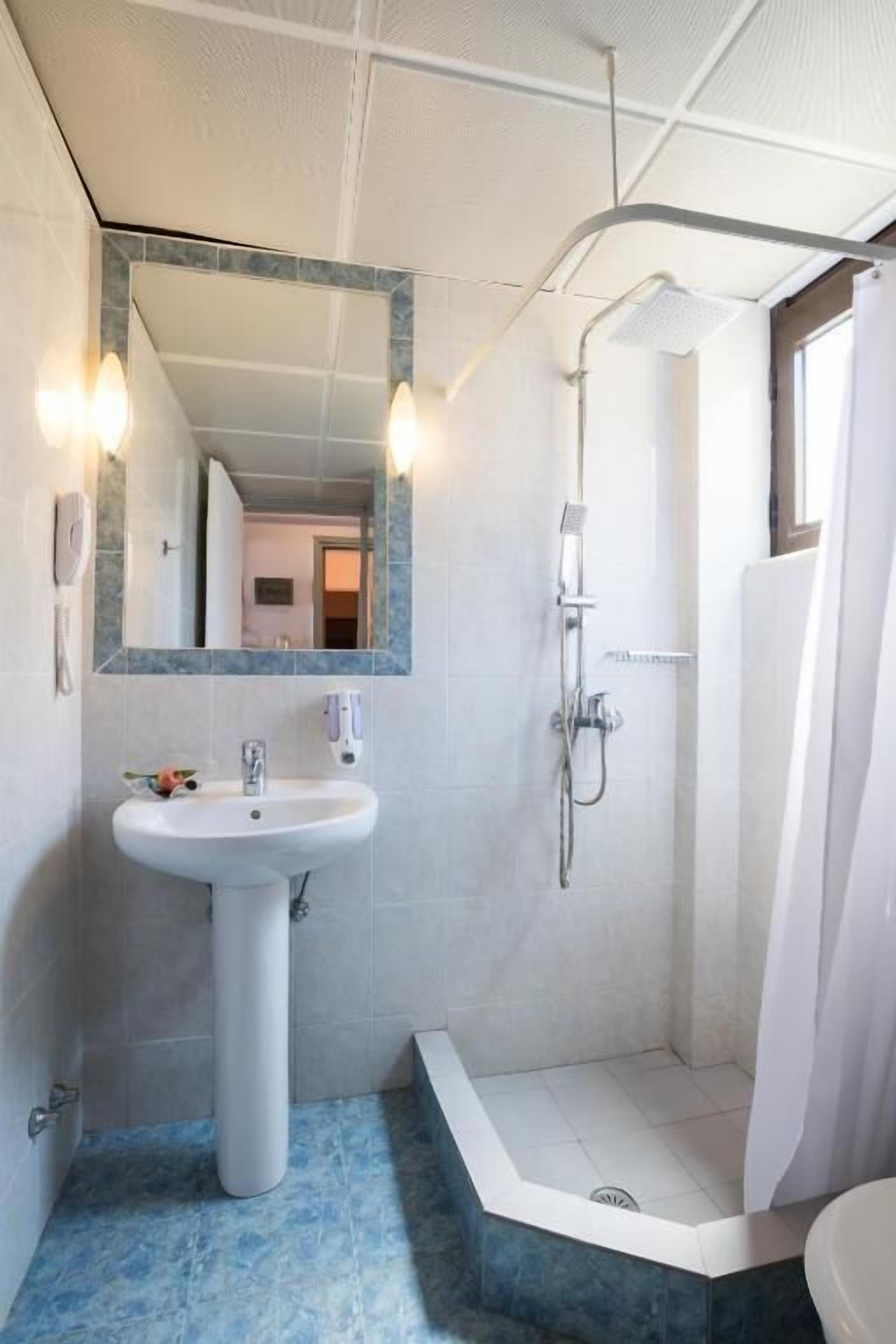 Un baño con lavamanos pedestal, cabina de ducha y espejo grande.