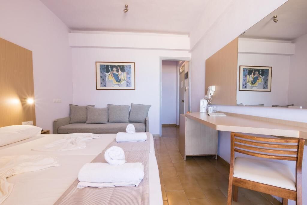 Een hotelkamer met twee bedden, een bank, een houten stoel, een bureau en een grote spiegel.
