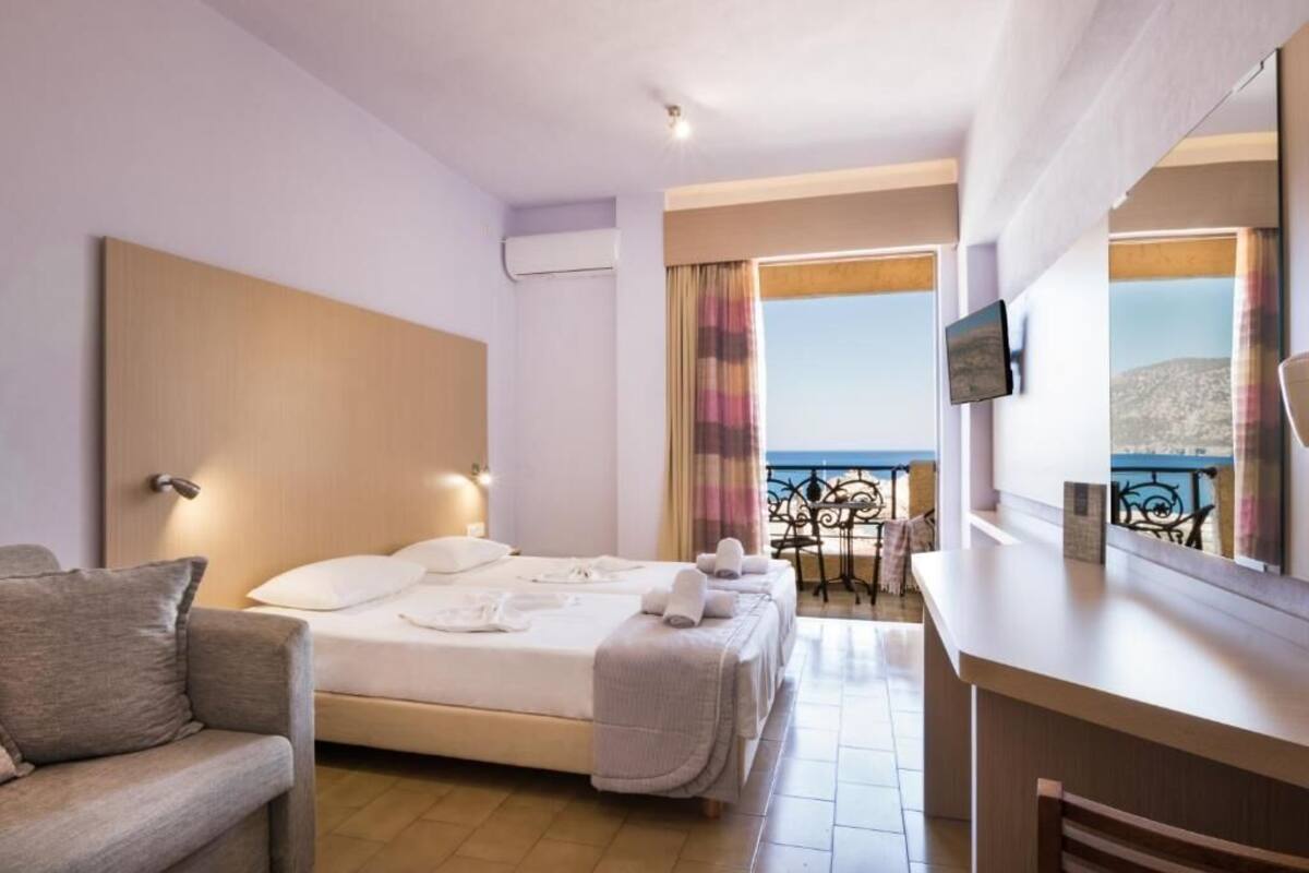 A hotel room with a bed, a sofa, a TV, and a balcony with a view of the sea.