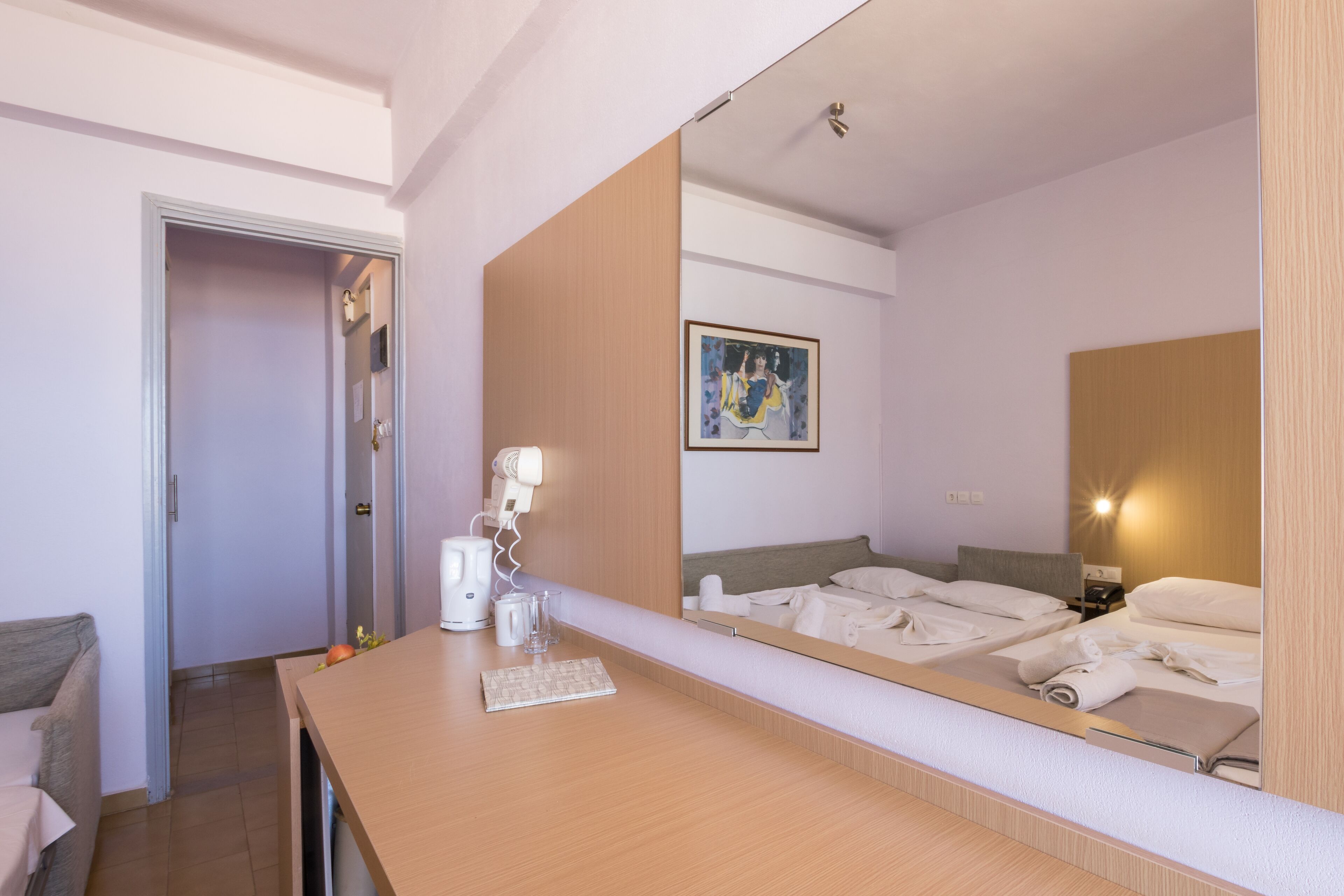 Ein Hotelzimmer mit Schreibtisch aus Holz, einem Bett mit weißen Leinentüchern, einem großen Spiegel und einem Bild an der Wand.