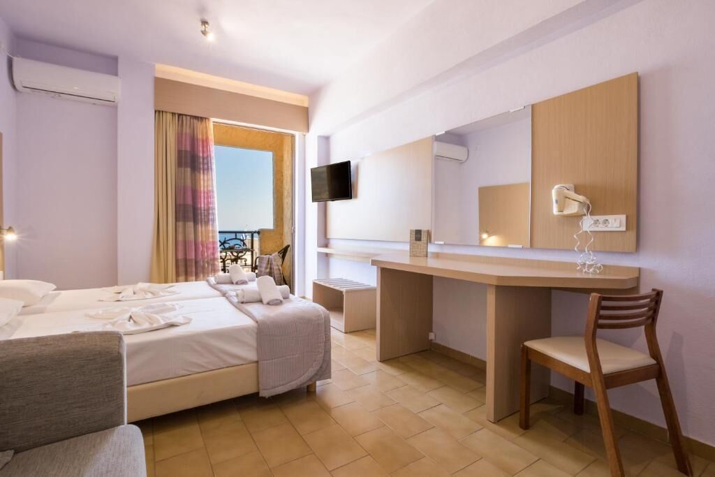 Une chambre d’hôtel avec un lit, un bureau, une chaise, une télévision et une fenêtre avec des rideaux.