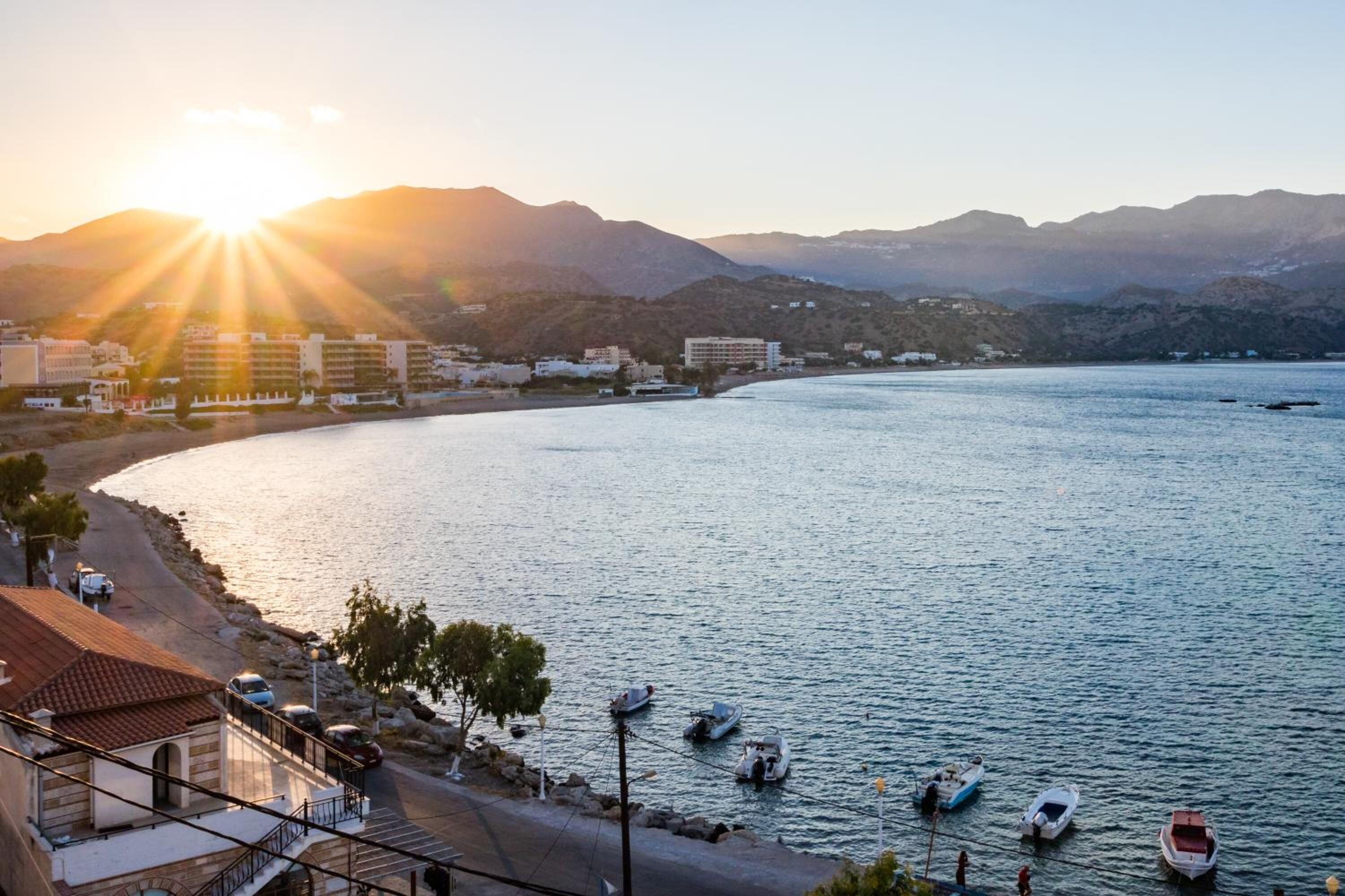 A coastal view with a marina, buildings, and mountains in the background.