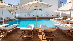 A poolside area with wooden loungers and umbrellas, surrounded by white buildings. - Atlantis Hotel (Karpathos)