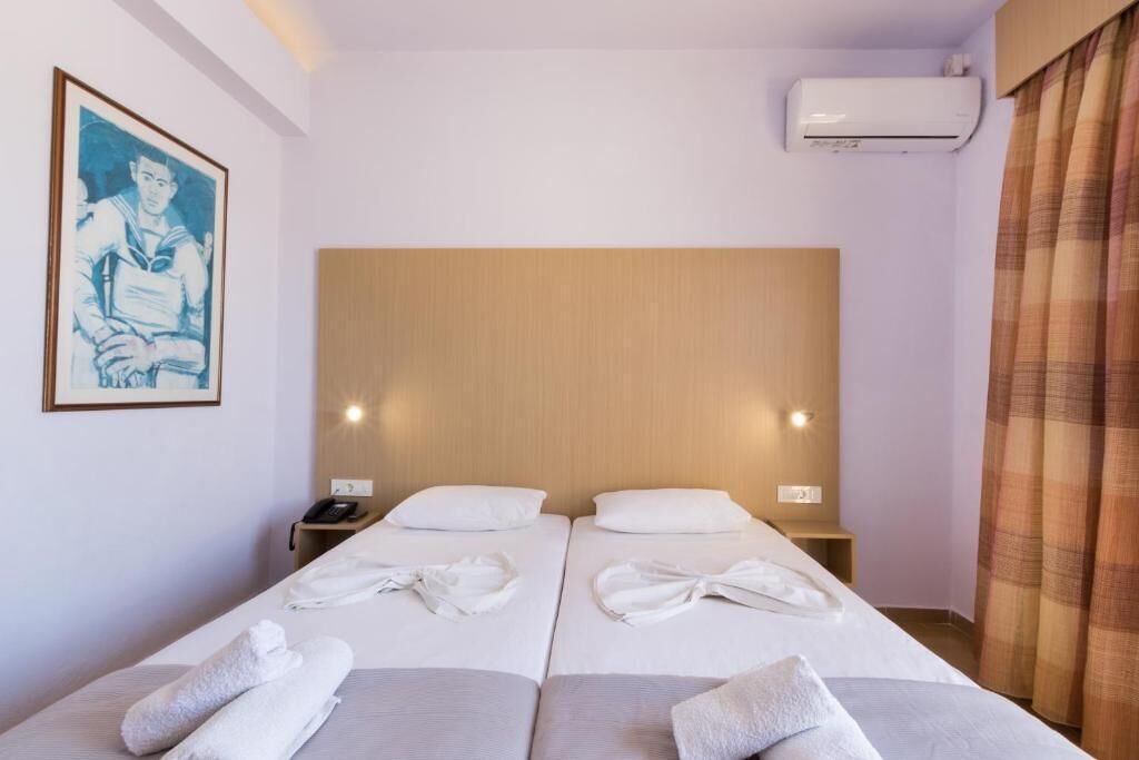 A hotel room with two beds, a wooden headboard, an air conditioning unit, a painting on the wall, and a telephone on the nightstand.