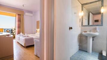 Habitación de hotel con cama, zona de estar con mesa y sillas, baño con lavabo y espejo, y vistas al exterior.